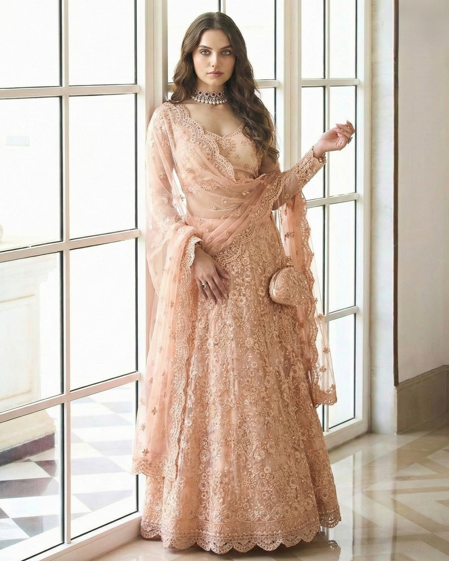 Woman in a peach lace dress standing in a room with large windows.