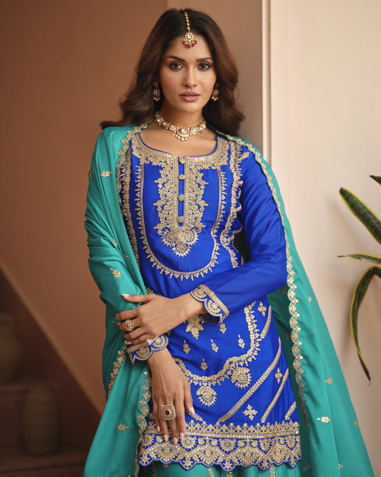 Woman wearing a blue and green traditional outfit with gold embroidery.