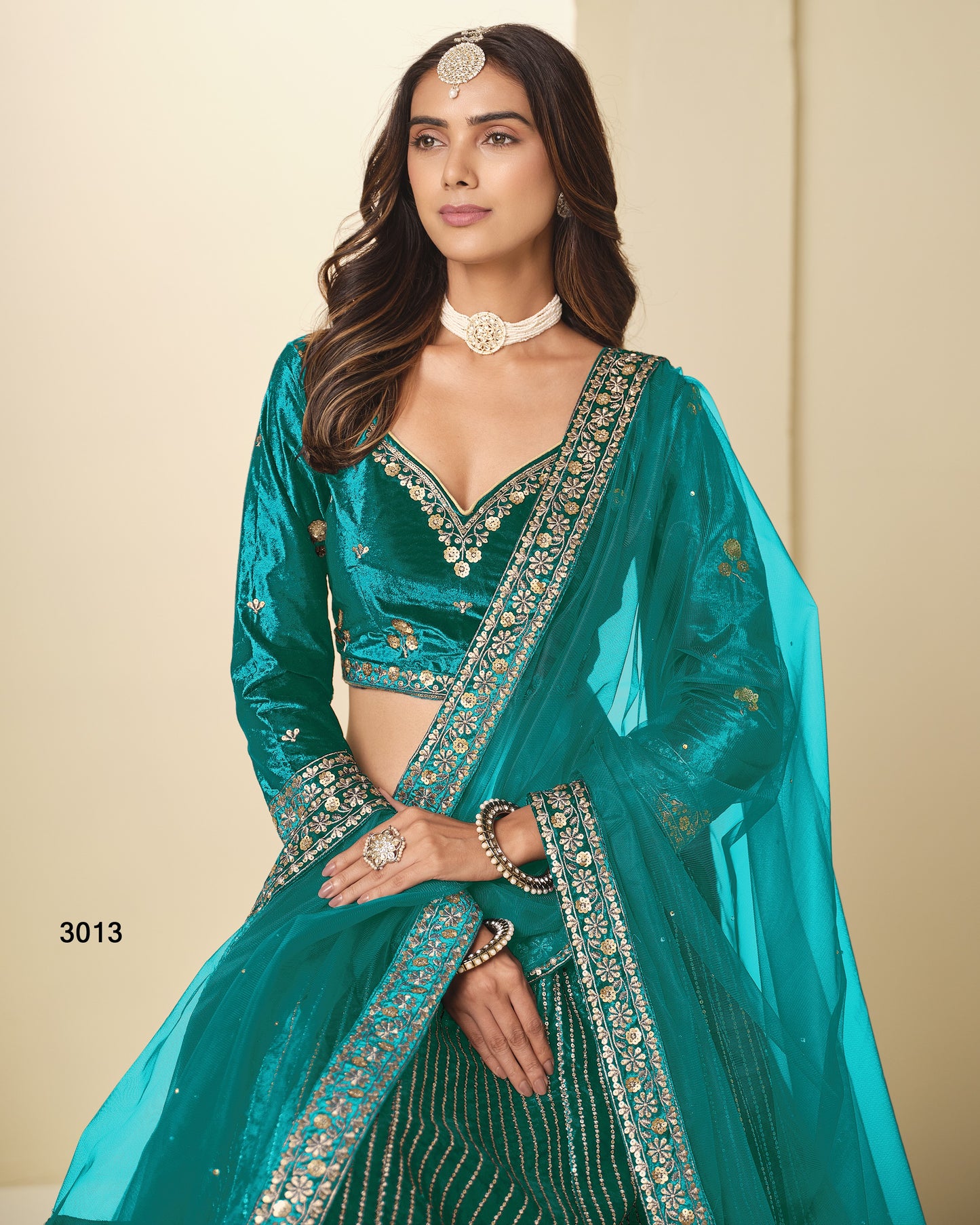Woman wearing a teal traditional outfit with intricate designs on a beige background