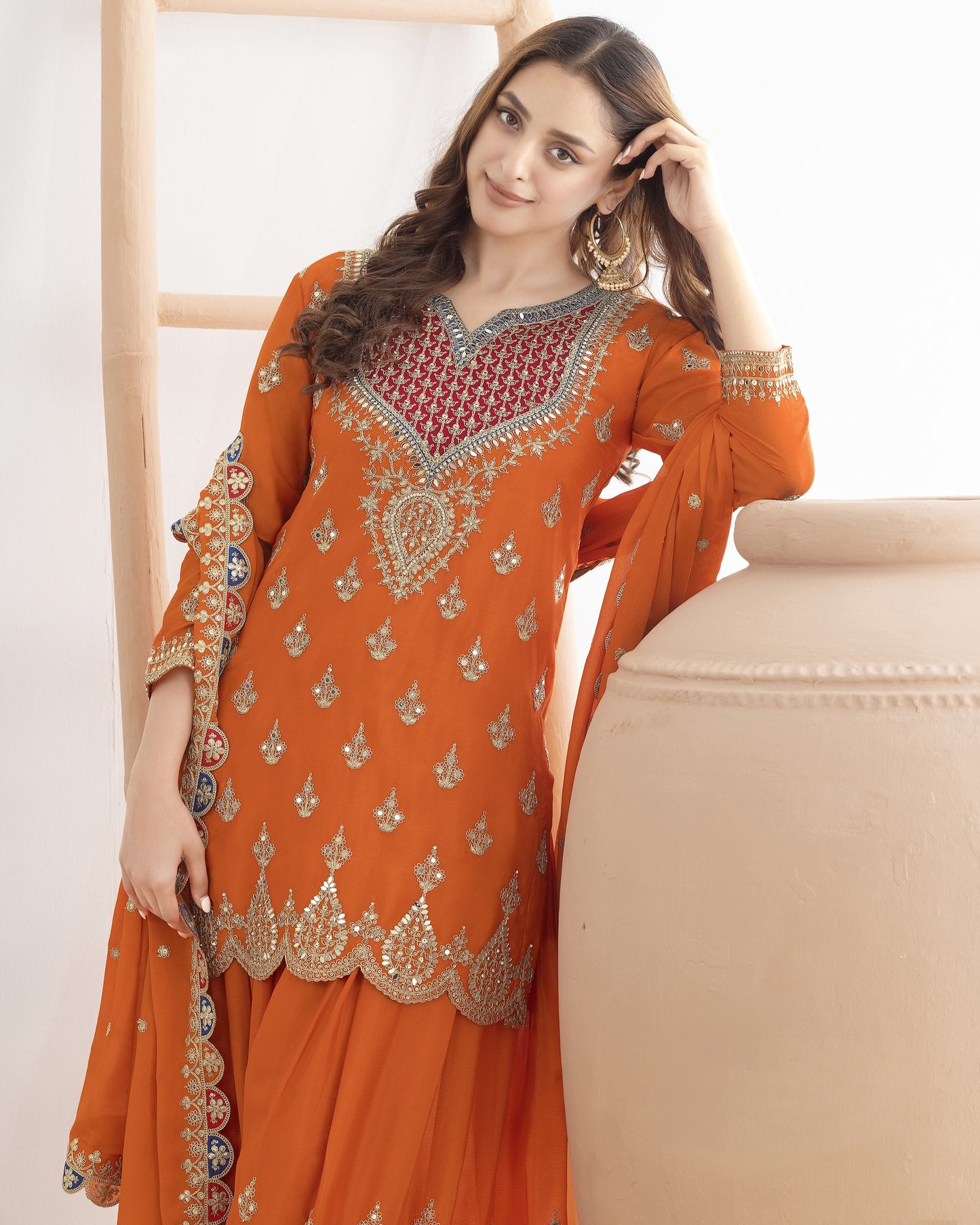 Woman wearing an orange embroidered traditional outfit against a beige background