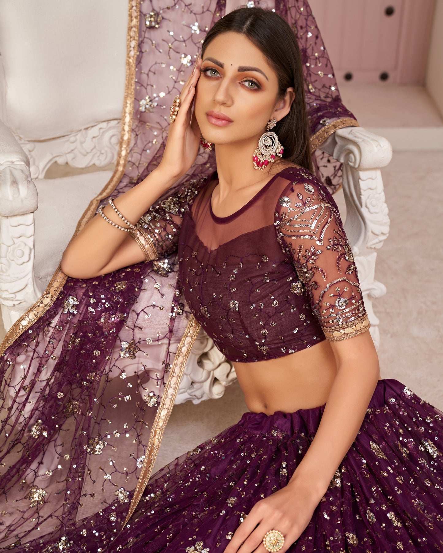 Woman in a purple embroidered outfit sitting on a decorative chair.