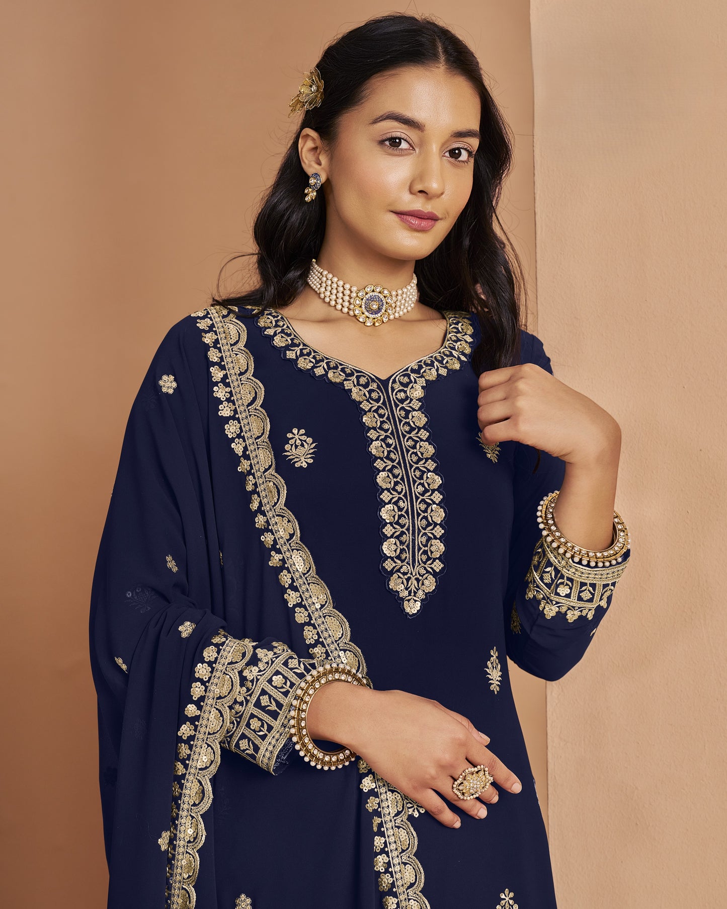 Woman wearing a navy blue embroidered outfit with gold details on a beige background