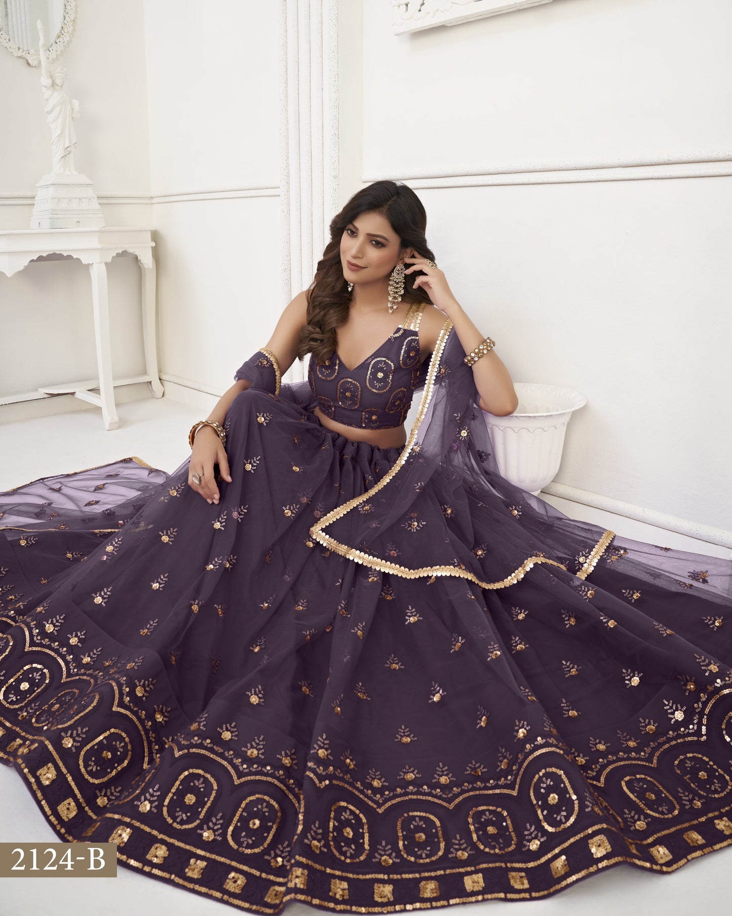 Woman in a dark purple embroidered traditional outfit sitting on a white couch.