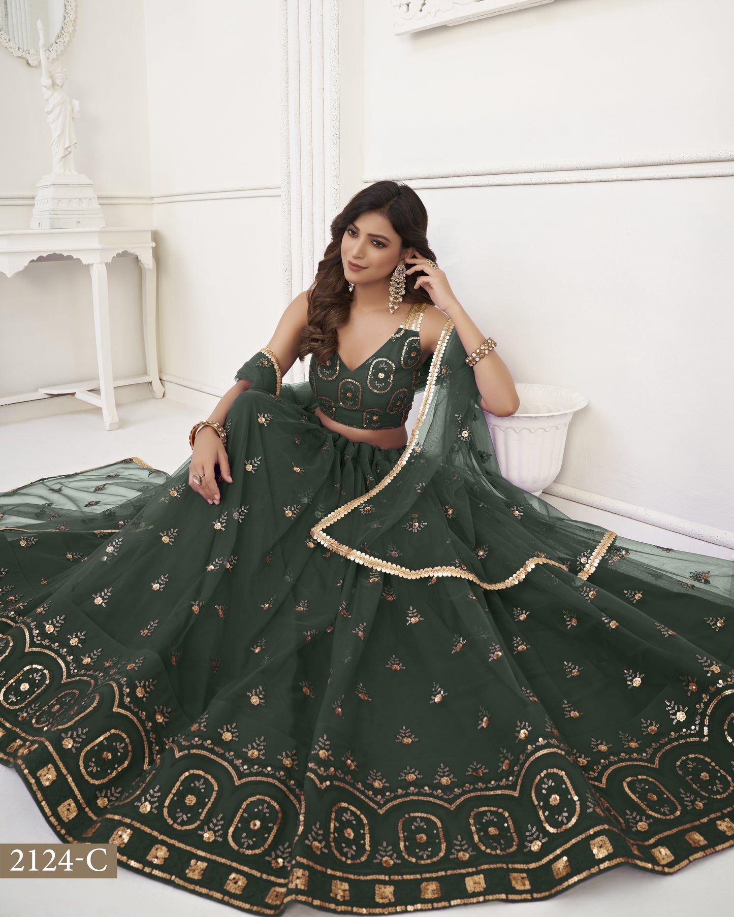 Woman in a dark green embroidered lehenga sitting on a white couch.