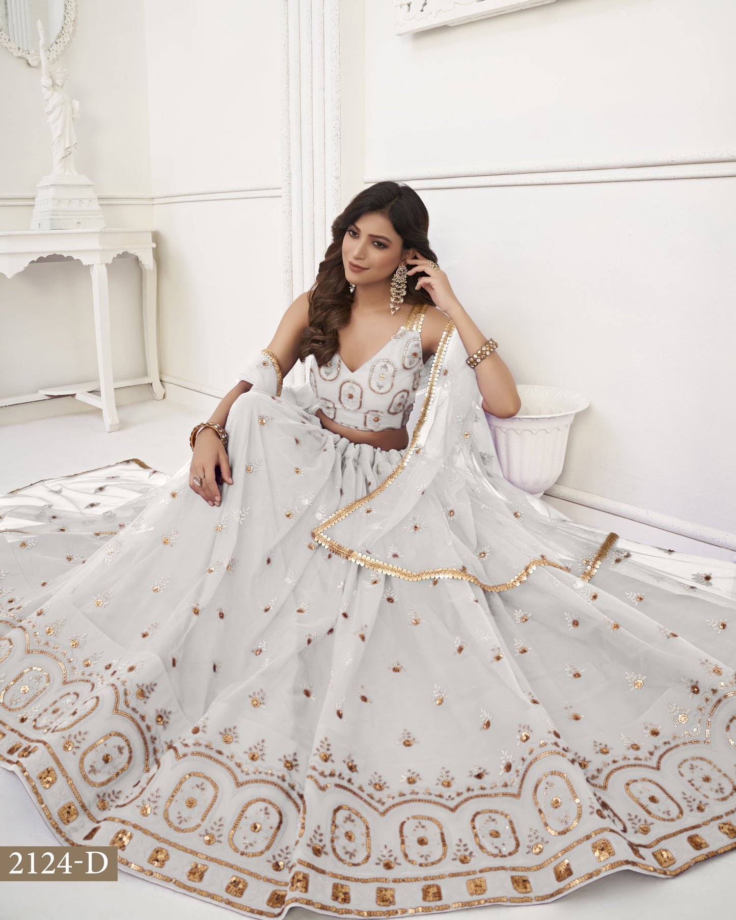 Woman in a white and gold embroidered saree sitting on a white couch.
