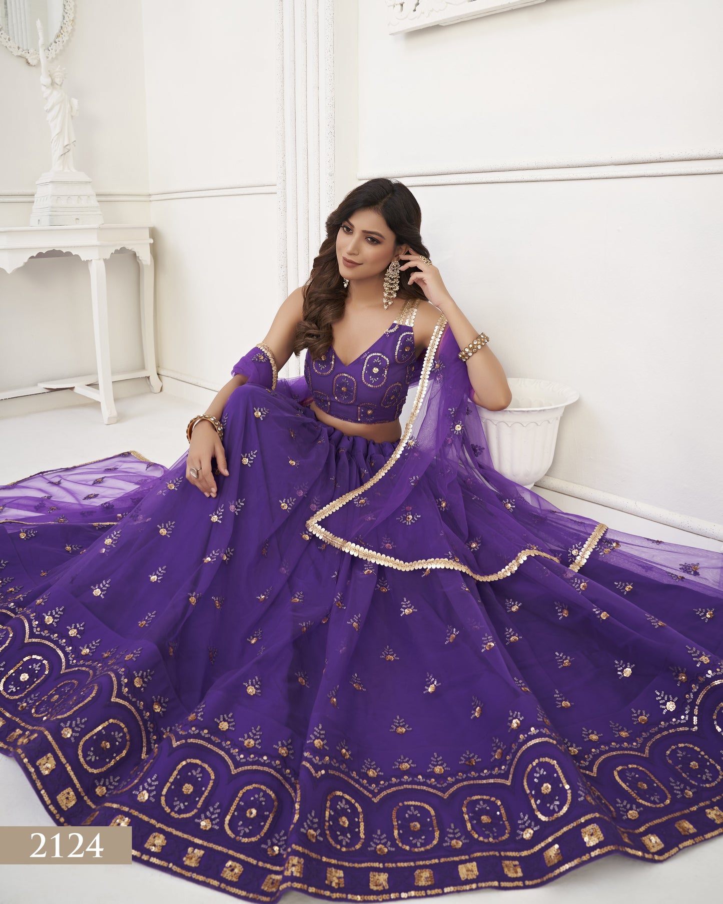 Woman in a purple embroidered traditional outfit sitting on a white couch.