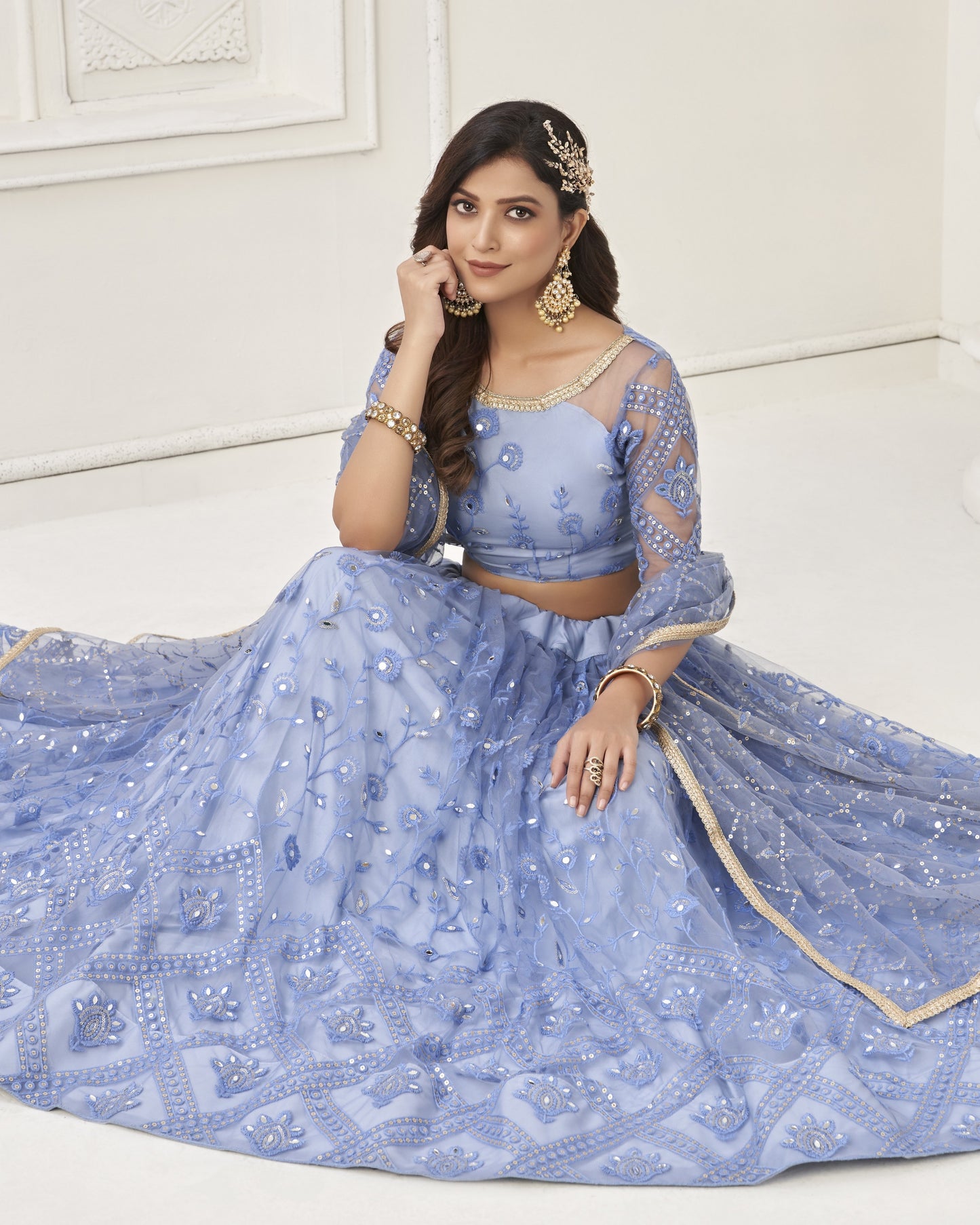 Woman wearing a blue embroidered lehenga with gold details against a white background