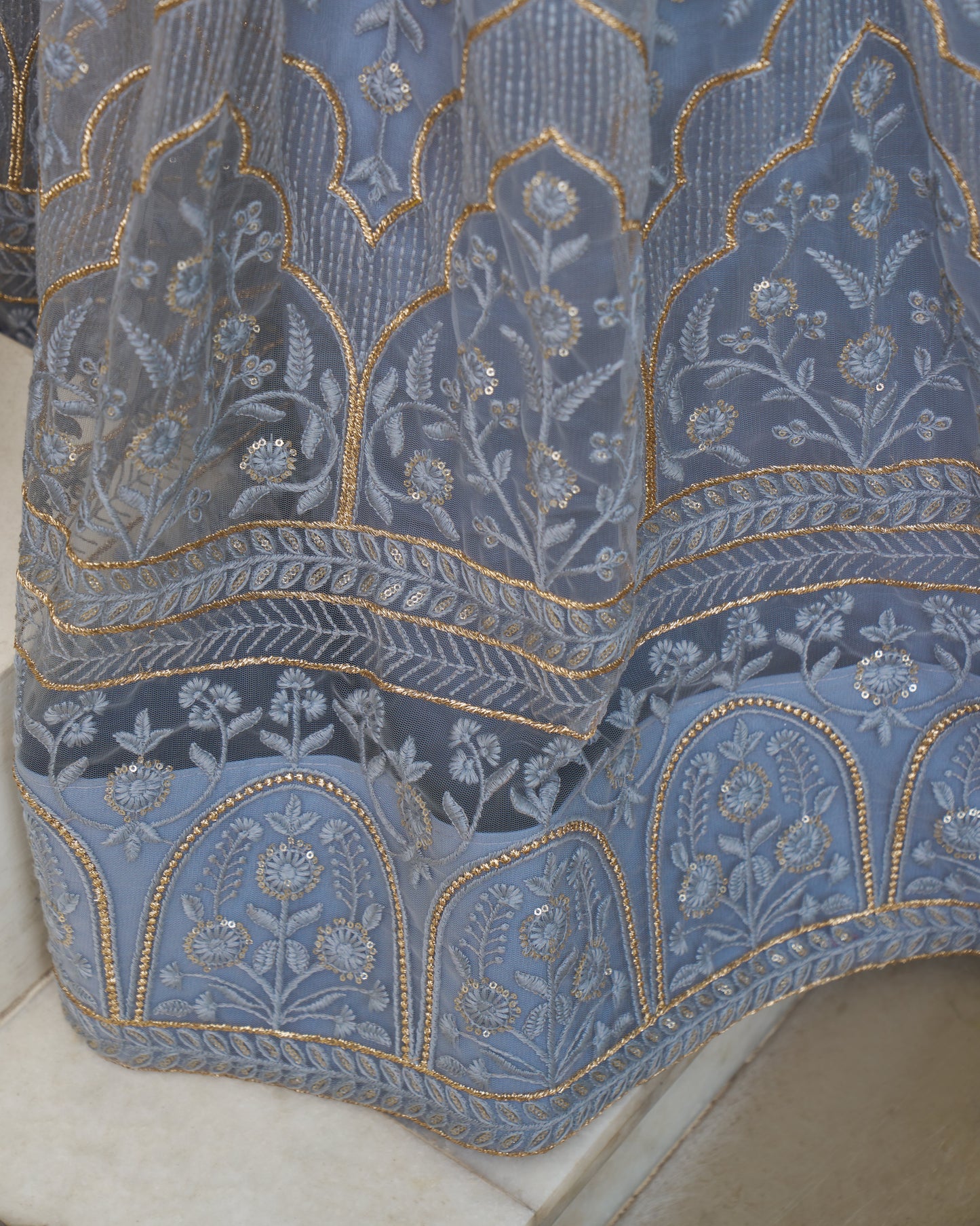 Close-up of a blue embroidered fabric with intricate patterns on a white background