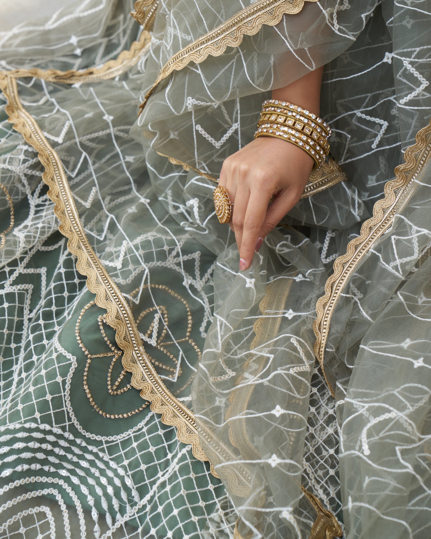 Close-up of a hand holding a sheer fabric with intricate patterns and gold lace trim.