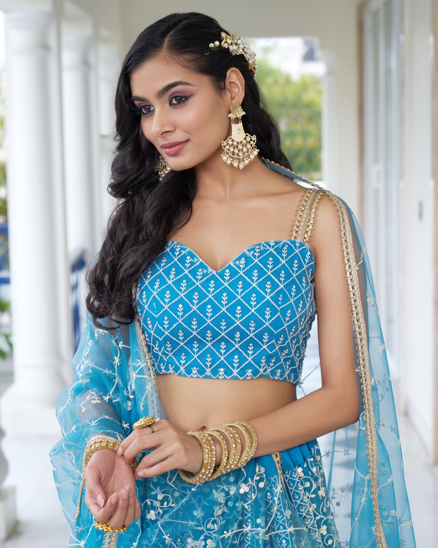 Woman wearing a blue traditional outfit with gold jewelry outdoors.