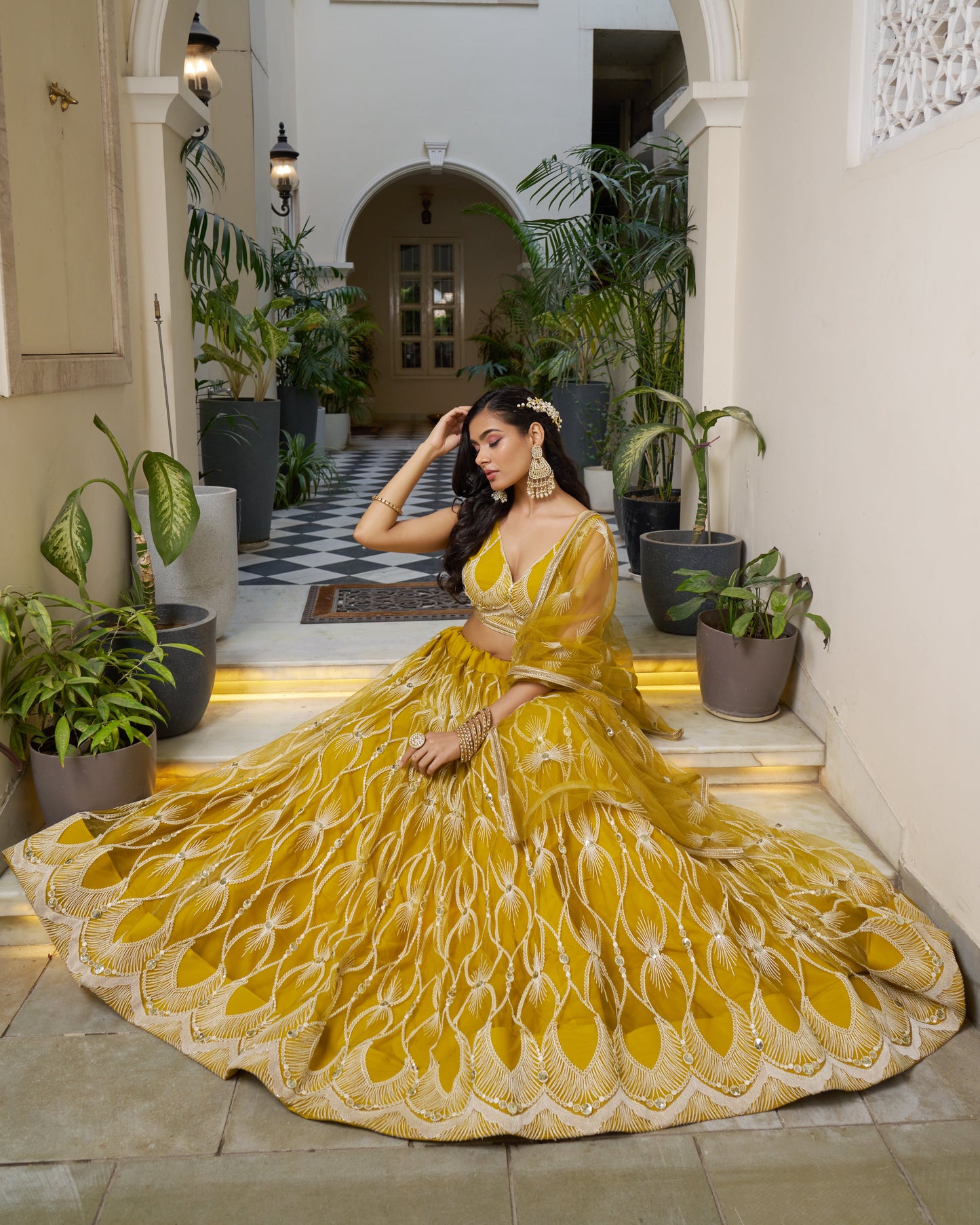 Woman in a yellow saree sitting in an indoor setting with plants