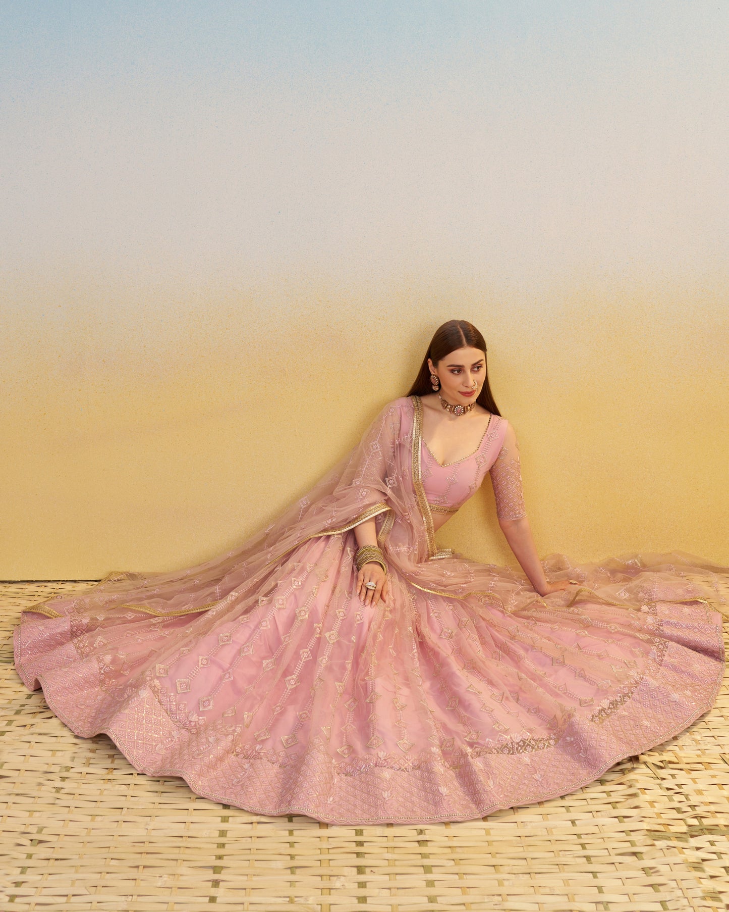 Woman in a pink traditional outfit with a flowing design against a gradient background