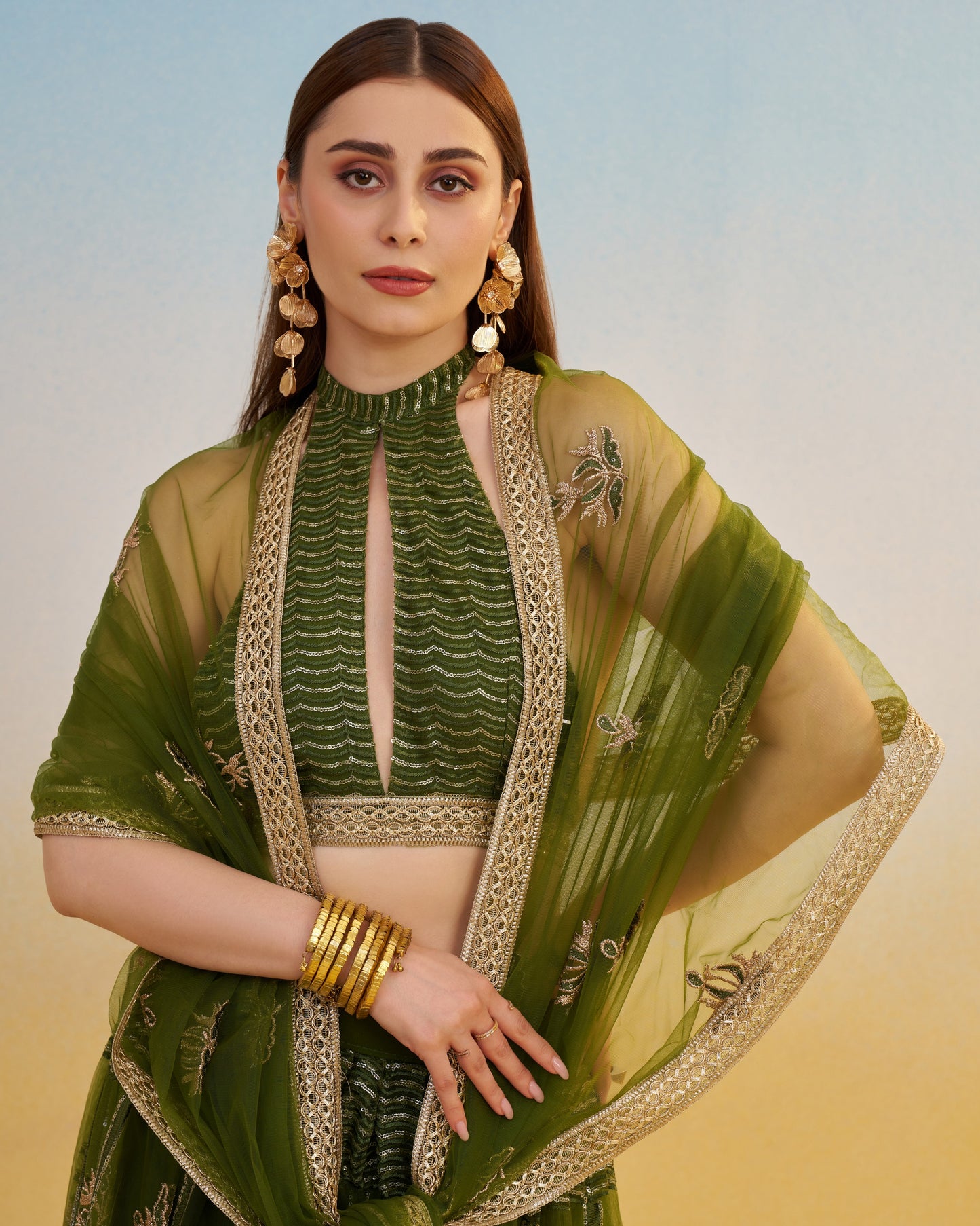 Woman wearing a green traditional outfit with gold embroidery against a gradient background