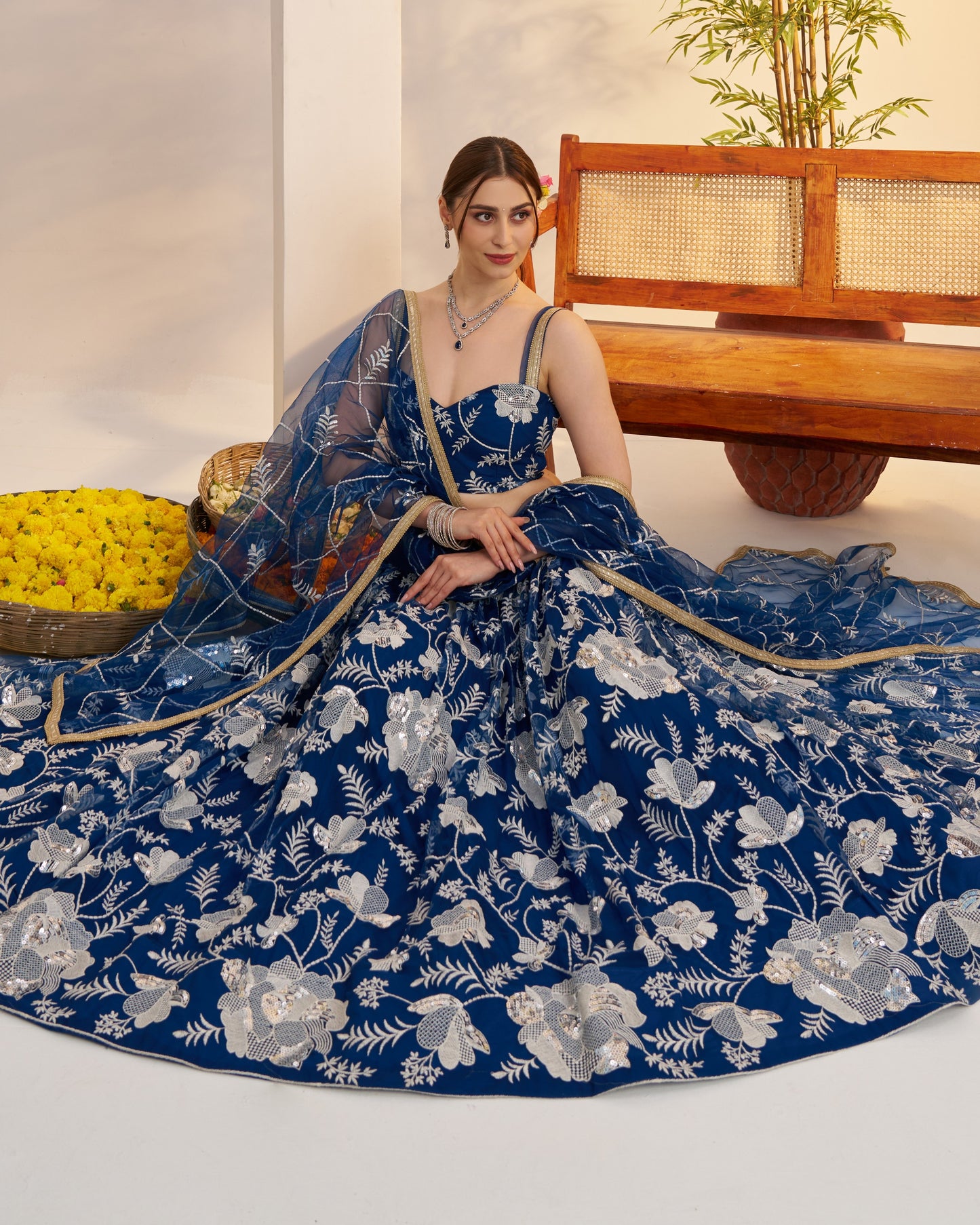 Woman in a blue floral dress sitting on the floor with a wooden bench and basket in the background.