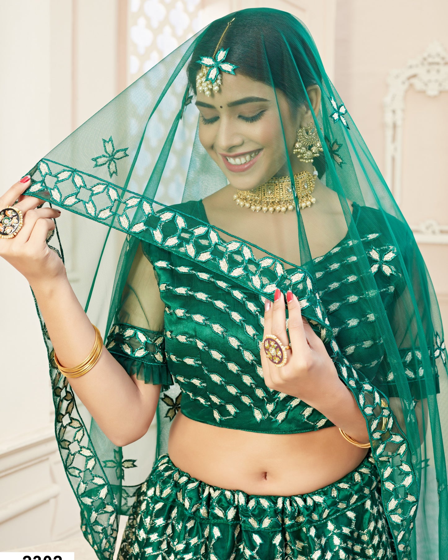 Woman wearing a green traditional outfit with a matching veil indoors.