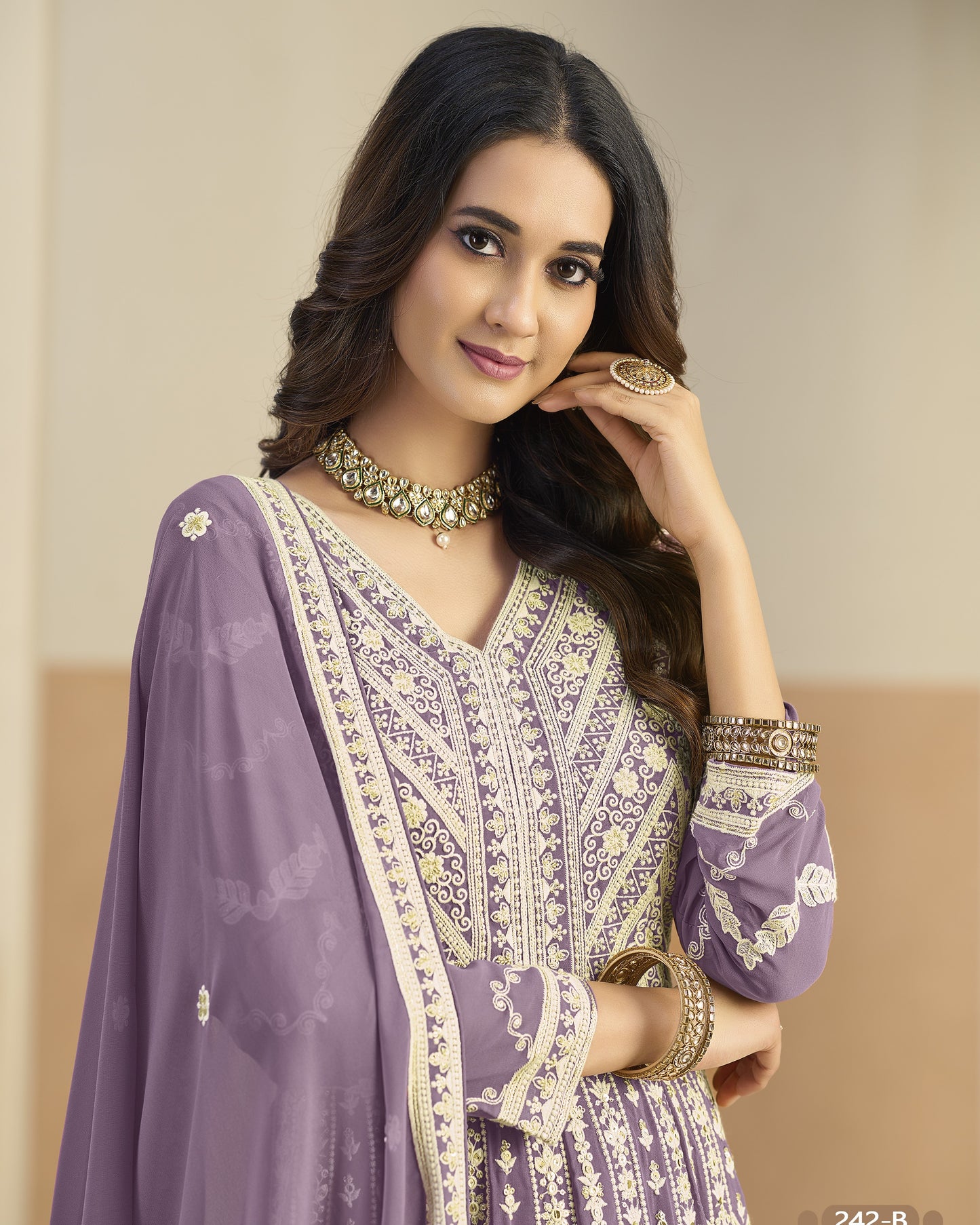 Woman wearing a purple and white embroidered traditional outfit with jewelry against a beige background