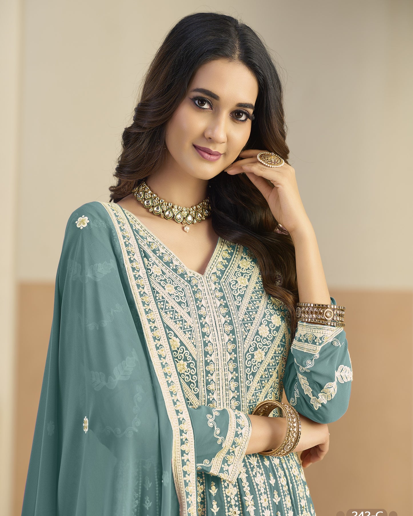 Woman wearing a traditional outfit with intricate designs and jewelry against a neutral background