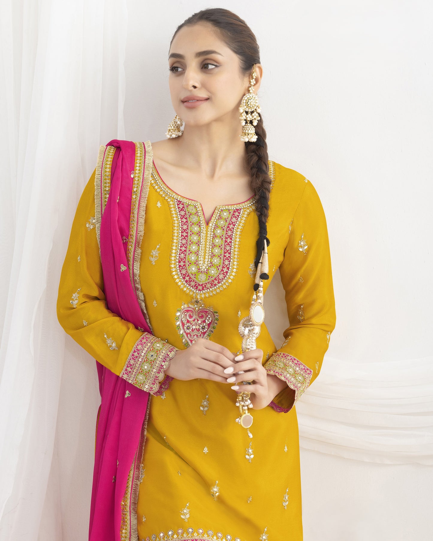 Woman wearing a yellow embroidered outfit with a pink dupatta against a white background