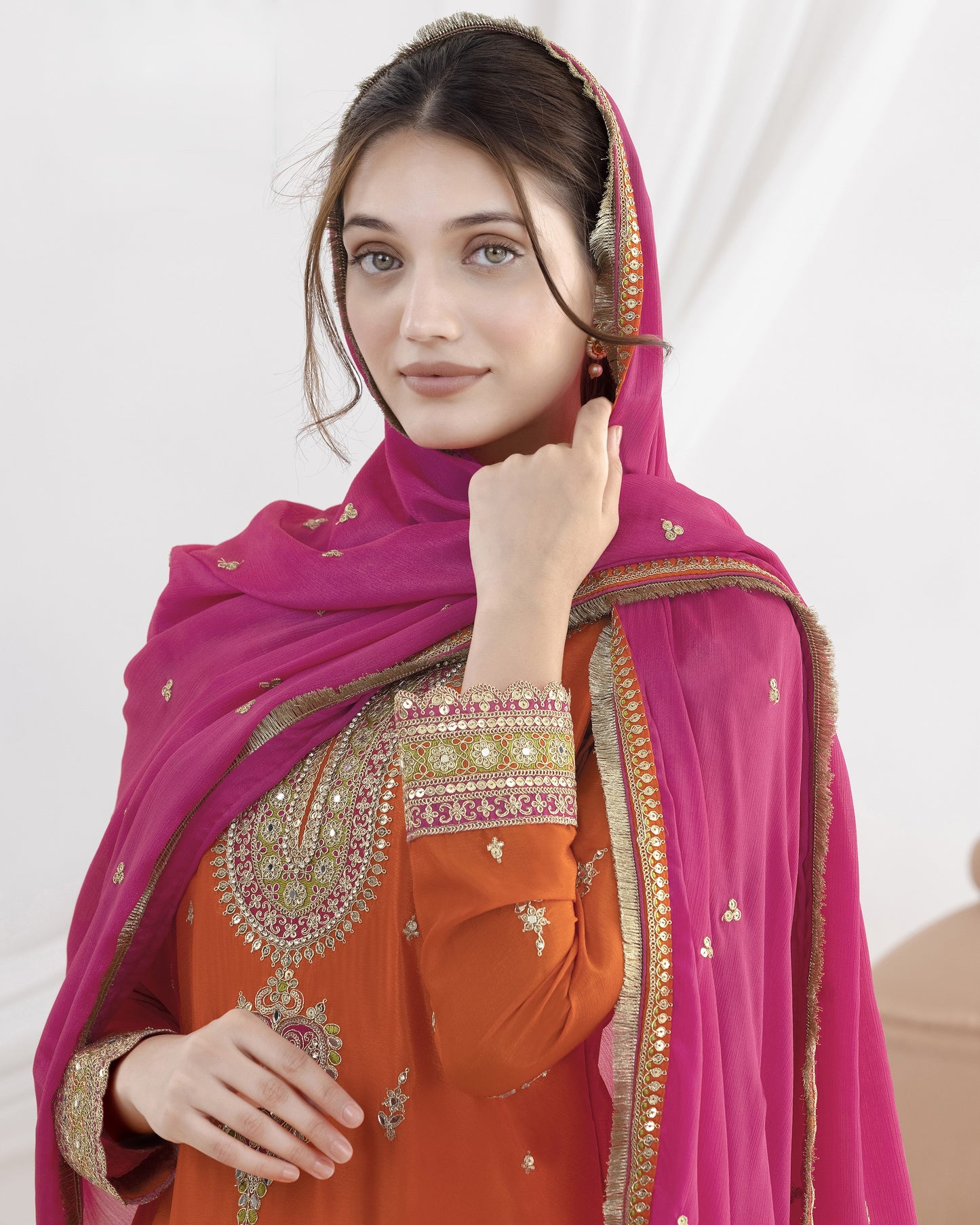 Woman wearing an orange outfit with a pink dupatta on a white background
