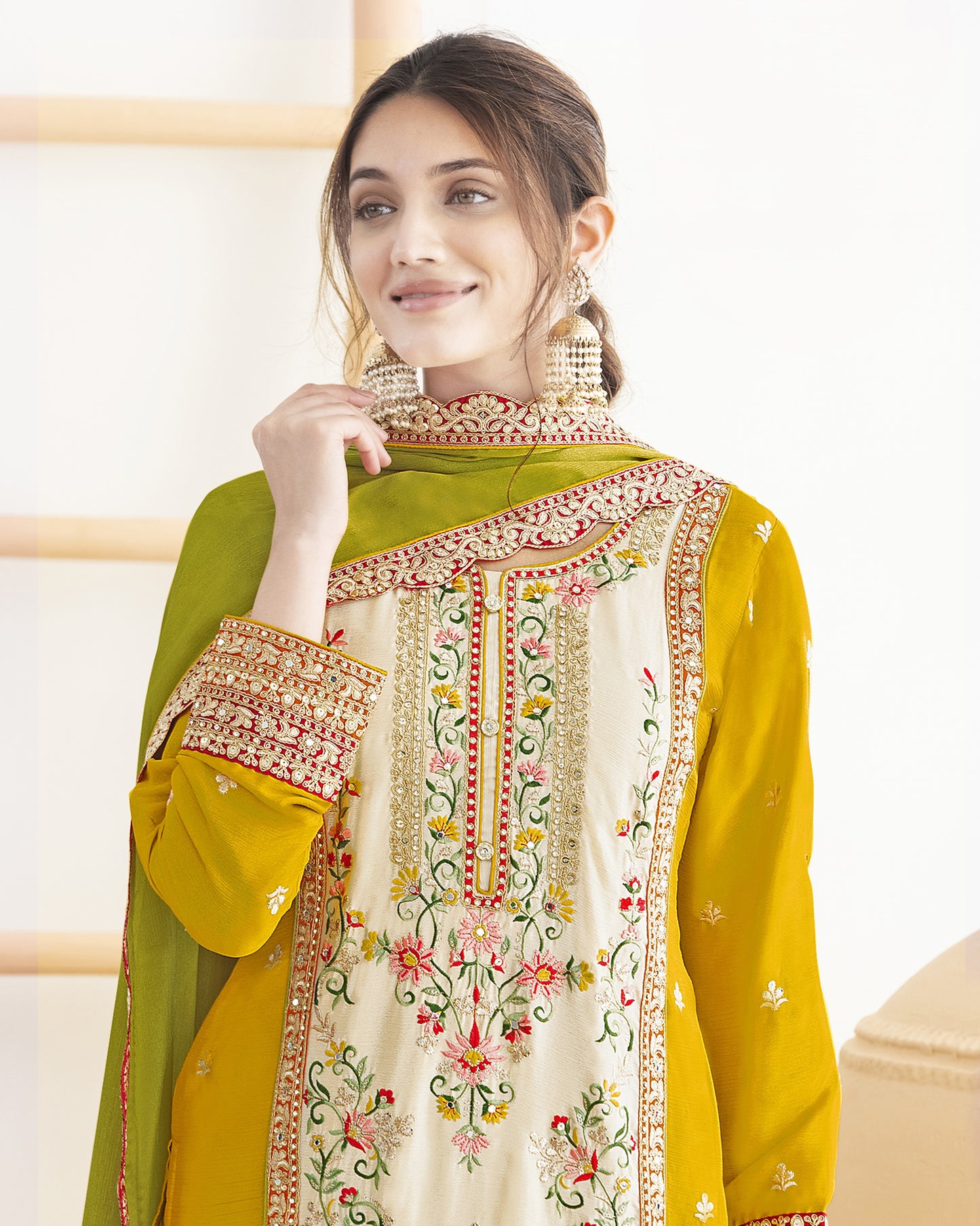 Woman wearing a green and yellow embroidered traditional outfit indoors.