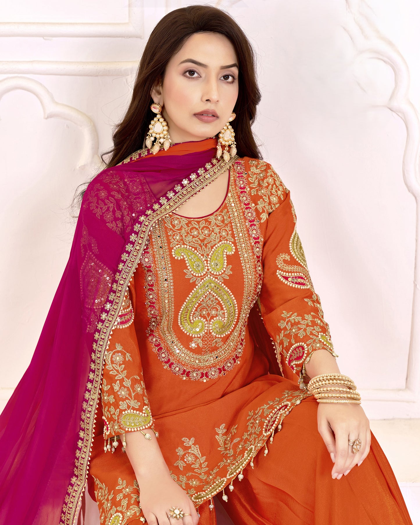 Woman wearing an orange and pink embroidered traditional outfit on a white background