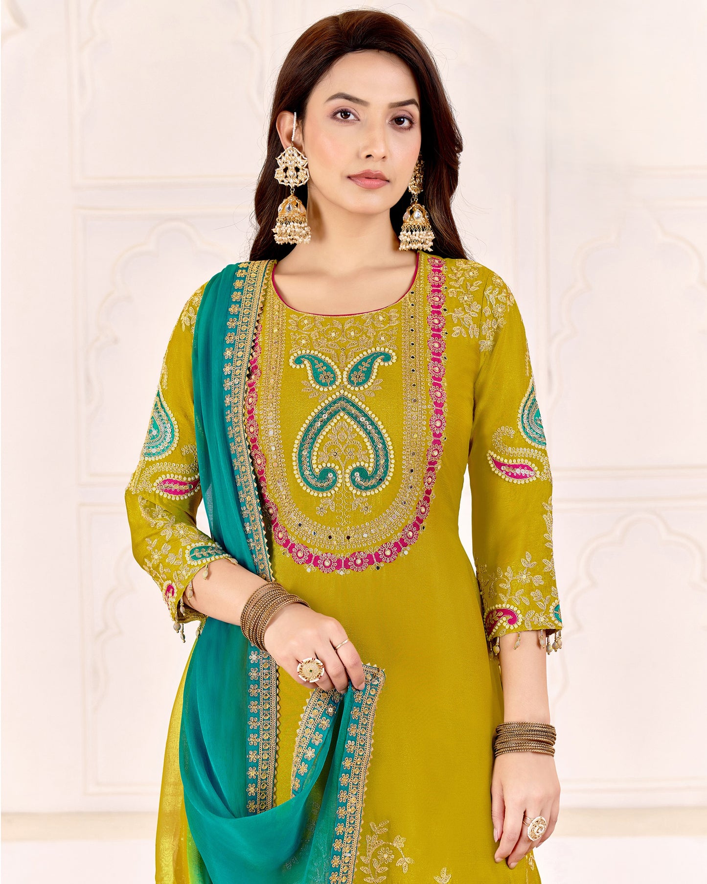 Woman wearing a green and teal embroidered traditional outfit on a white background