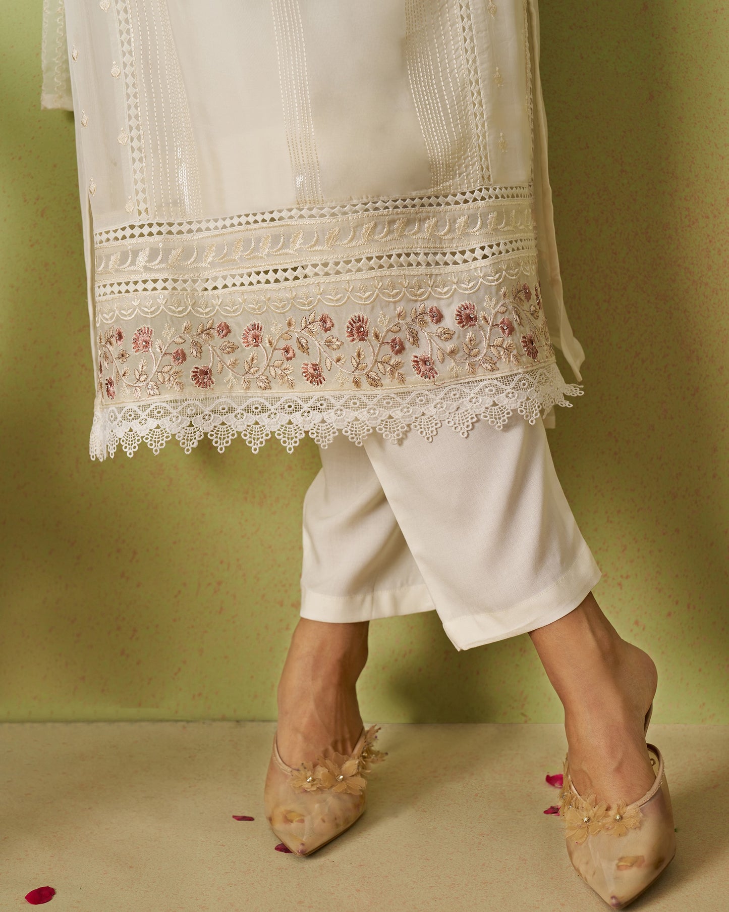 White embroidered kurta with matching pants and beige shoes on a green background