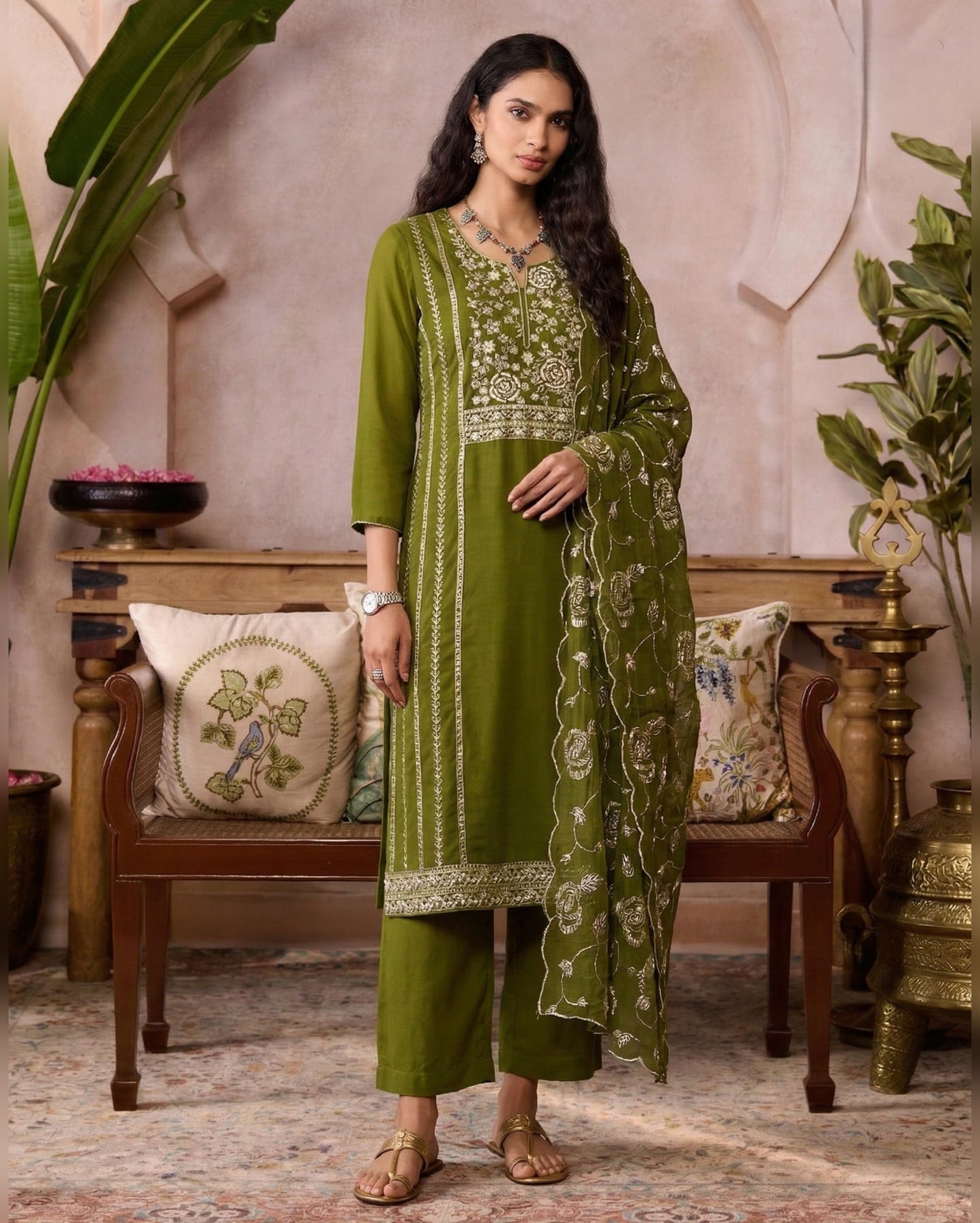 Woman wearing a green embroidered traditional outfit in a decorated room.
