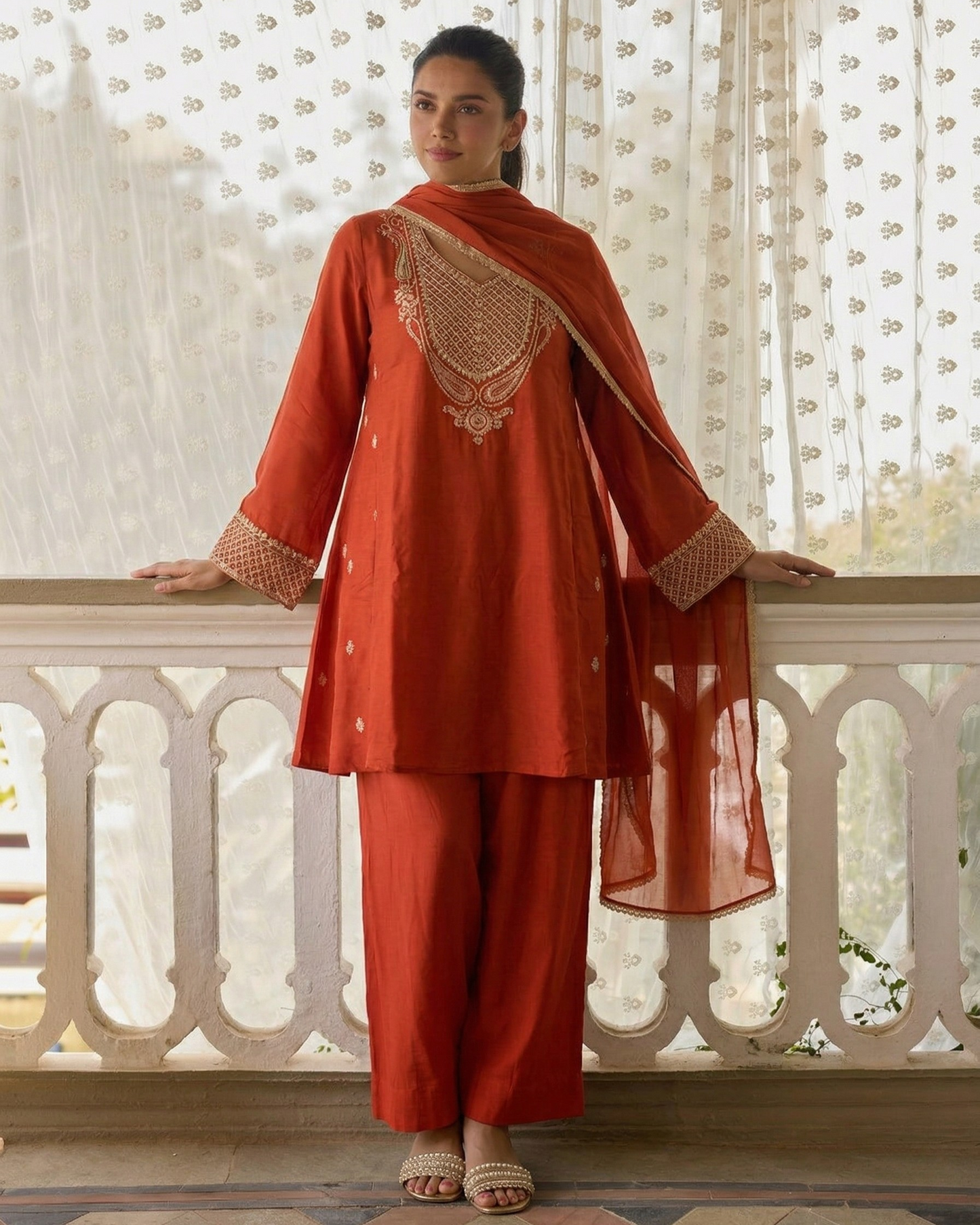 Woman wearing a traditional outfit with intricate patterns in a decorative setting.