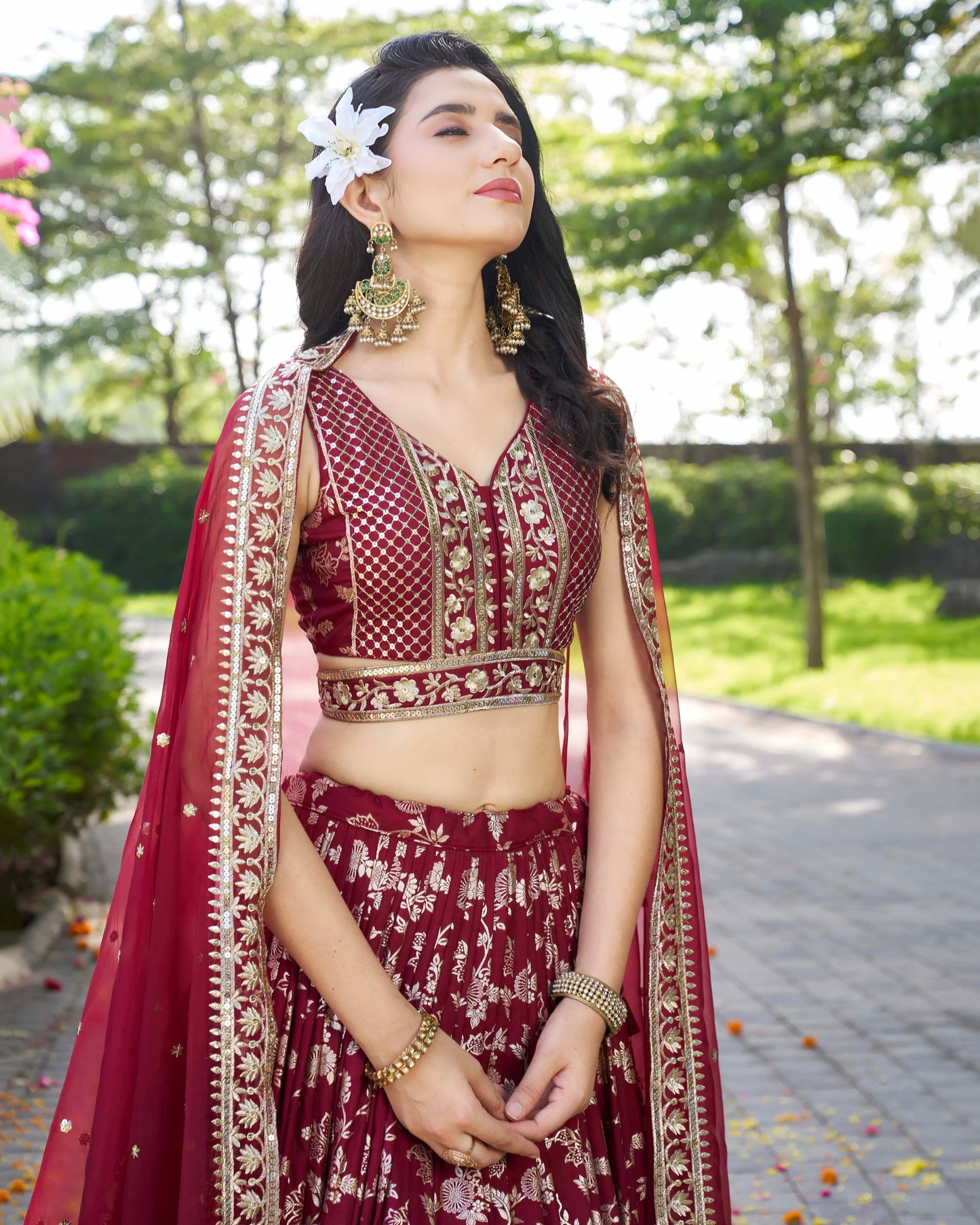 Woman in traditional maroon and gold outfit with floral hairpiece outdoors.