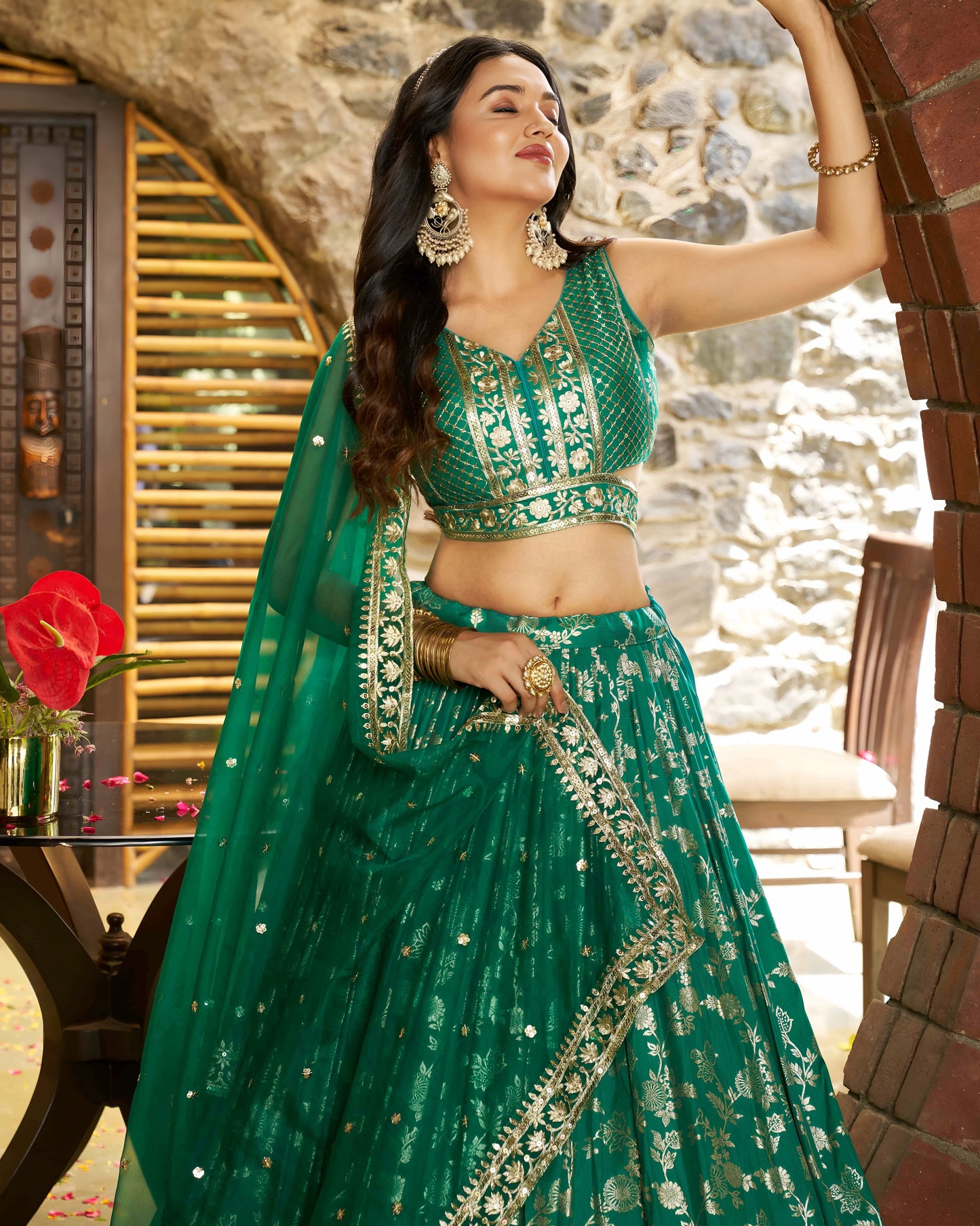 Woman in a green traditional outfit with intricate designs, standing in an outdoor setting.