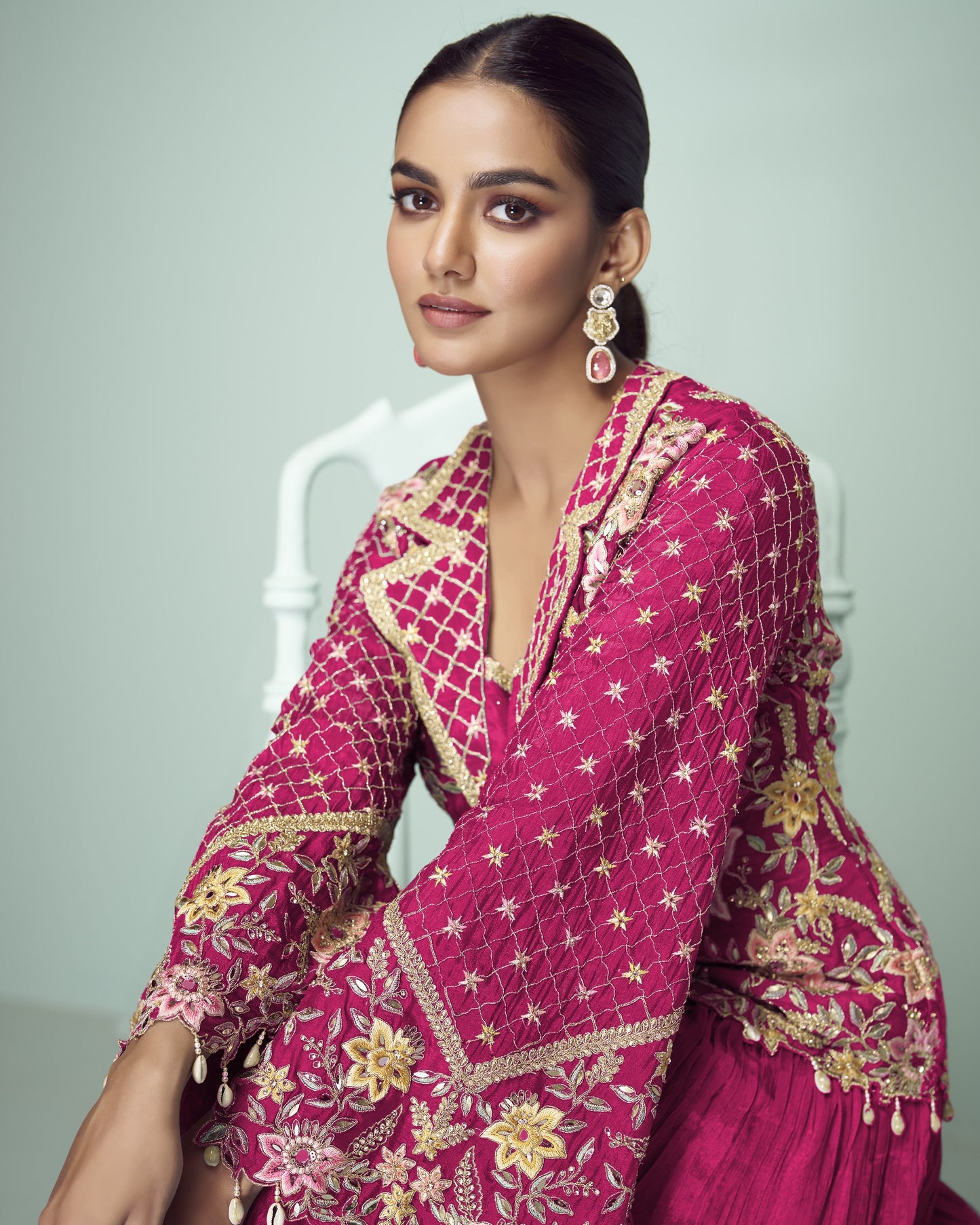 Woman wearing a pink embroidered traditional outfit with gold details on a light gray background