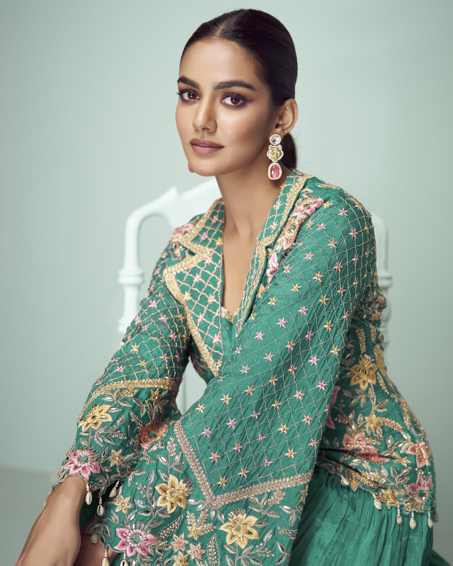 Woman wearing a green embroidered traditional outfit with a plain background