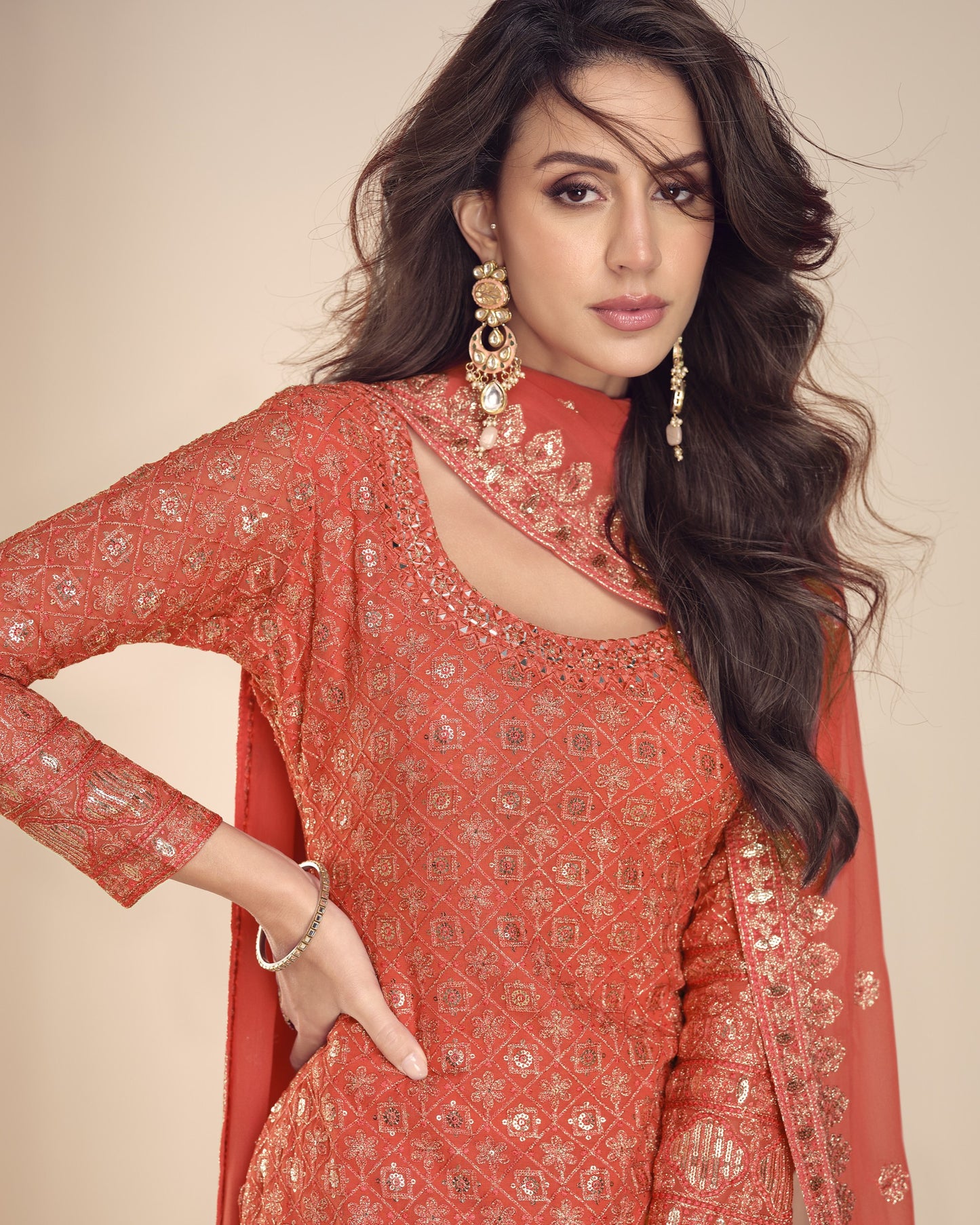 Woman wearing a red embroidered traditional outfit with gold jewelry against a beige background