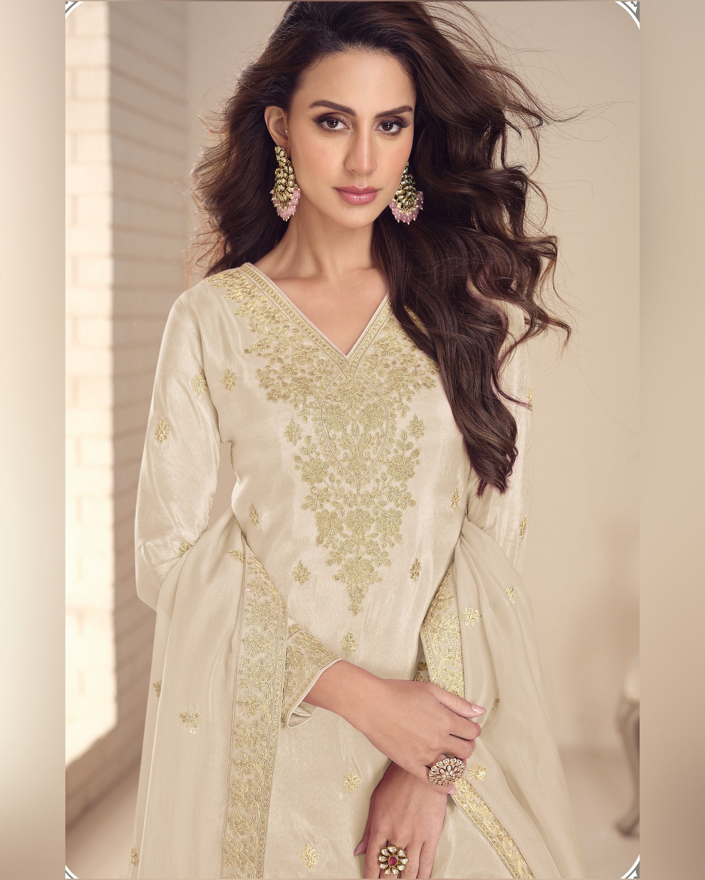 Woman wearing a beige embroidered traditional outfit with jewelry indoors.