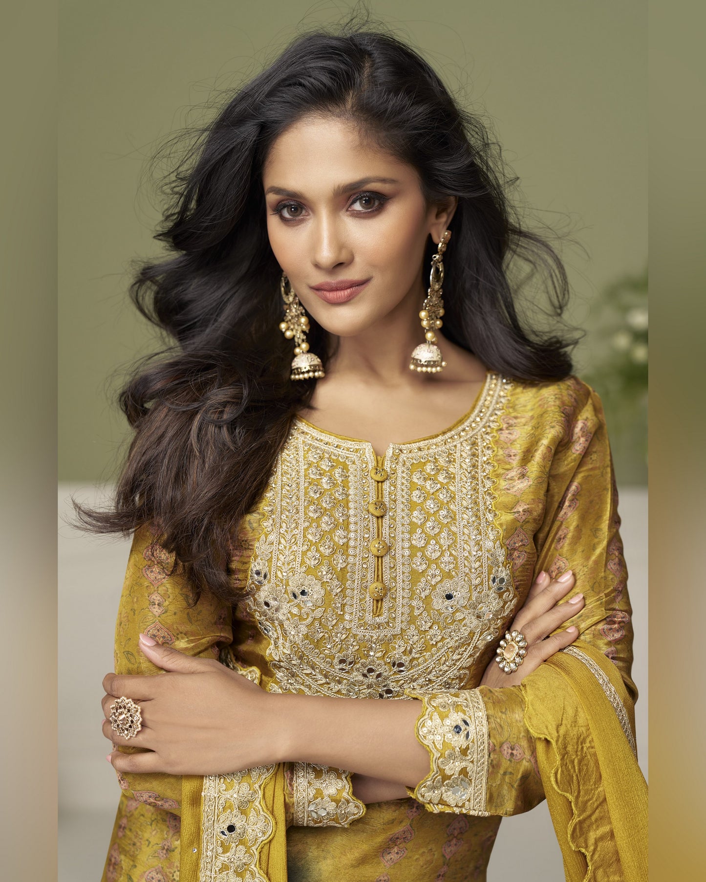 Woman wearing a yellow embroidered traditional outfit with jewelry against a neutral background