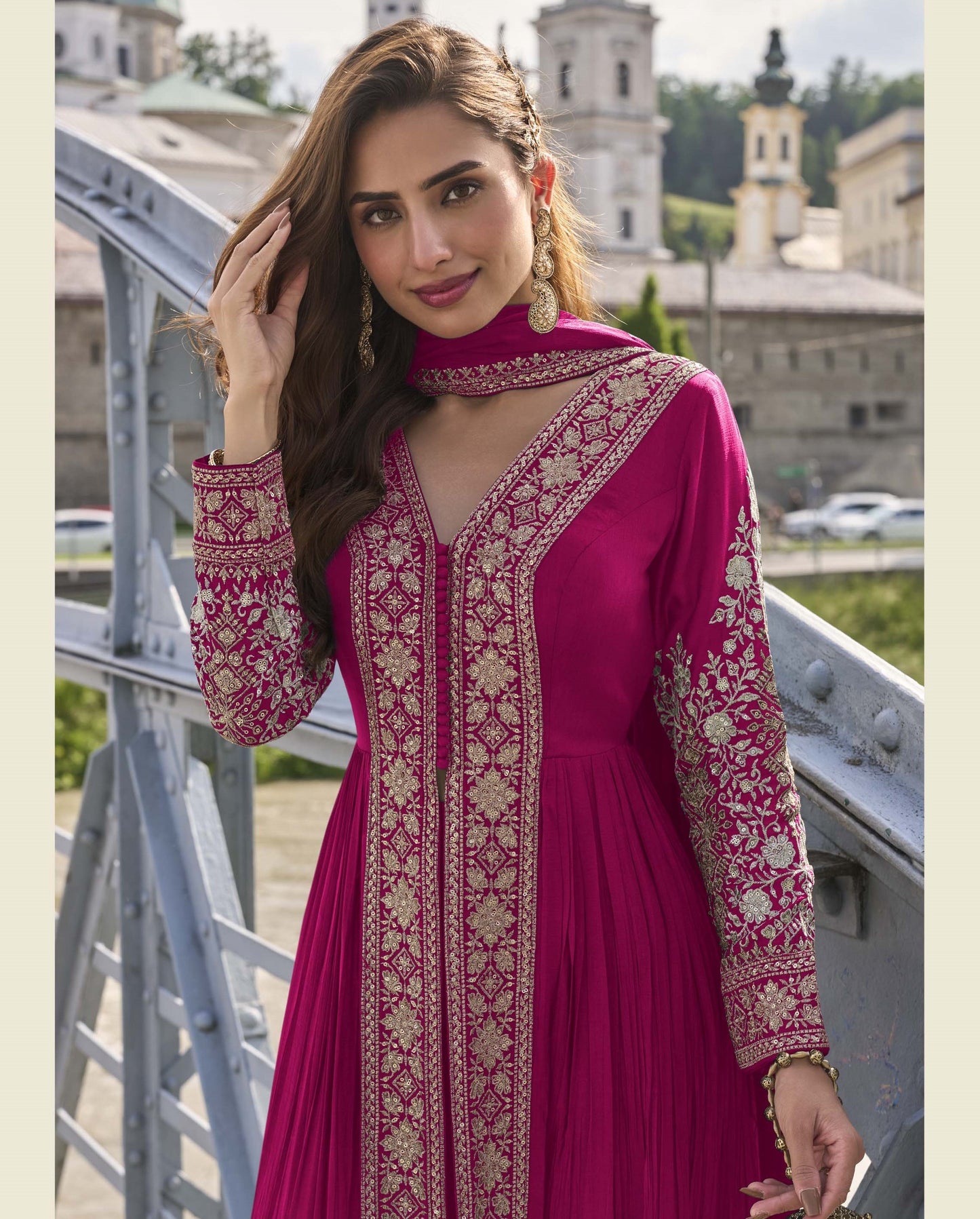 Woman in a pink embroidered dress standing outdoors with buildings in the background