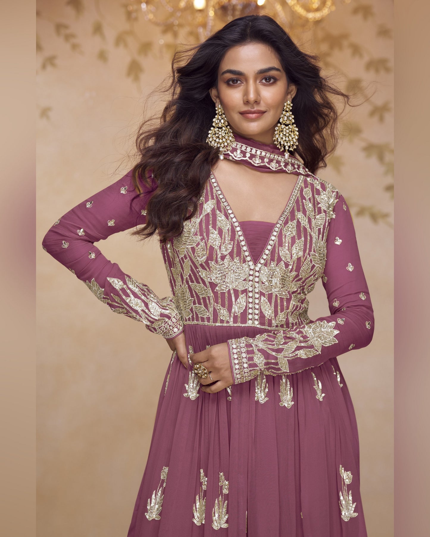 Woman wearing a purple embroidered outfit with gold jewelry against a beige background
