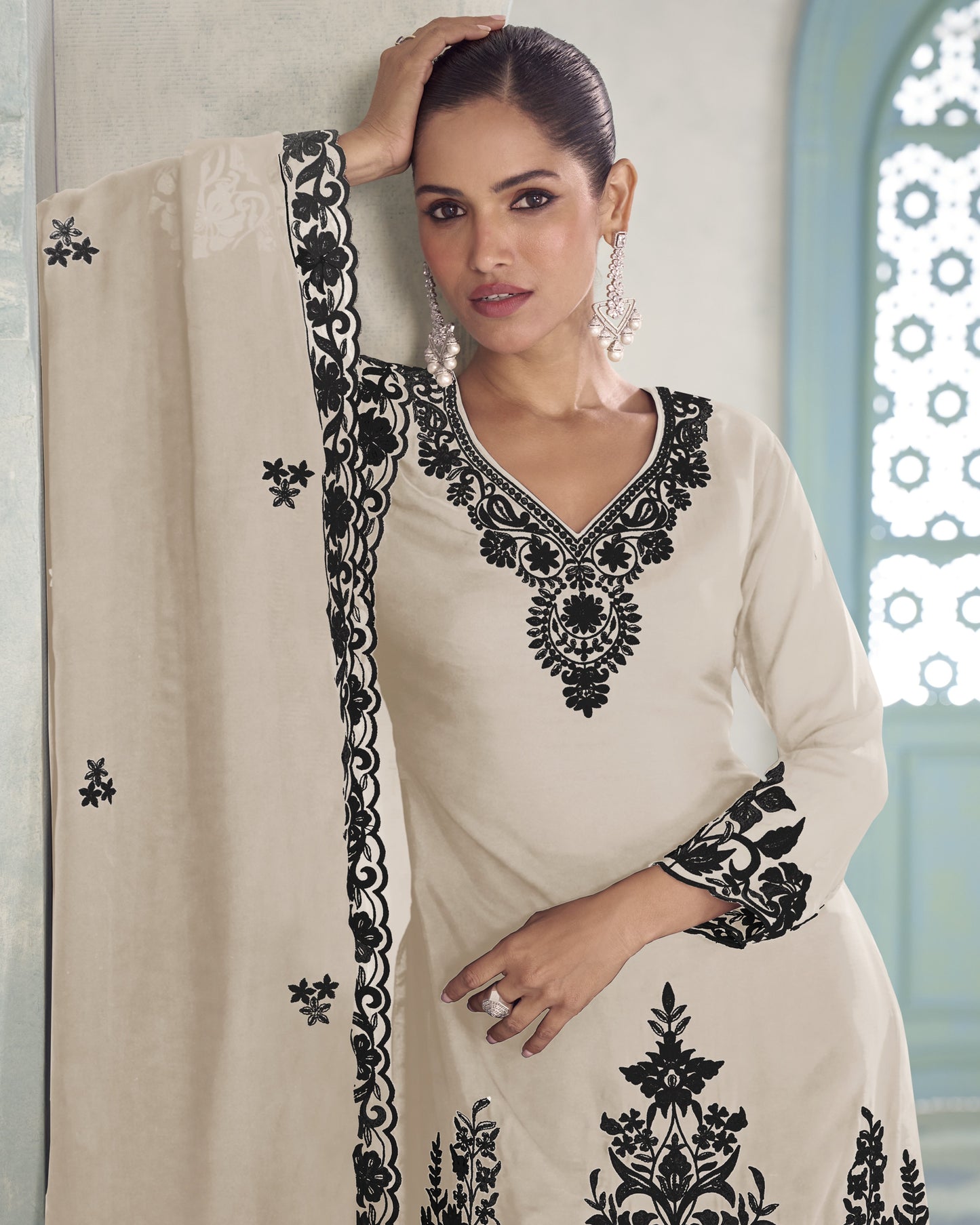 Woman wearing a cream-colored outfit with black embroidery against a neutral background