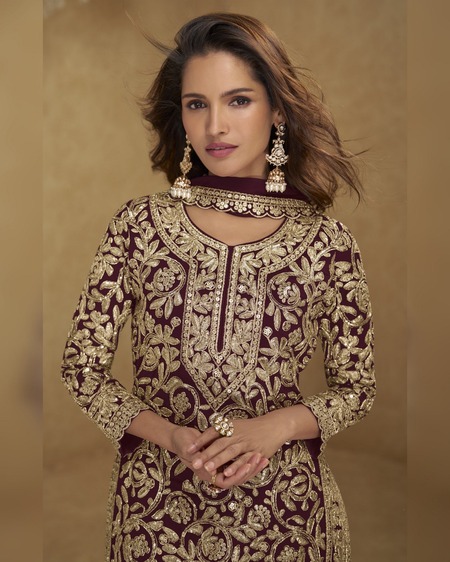 Woman wearing a maroon and gold embroidered traditional outfit against a beige background