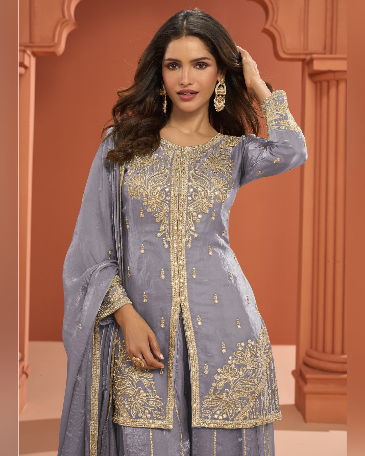 Woman wearing a gray embroidered traditional outfit with gold details against a warm-toned background.