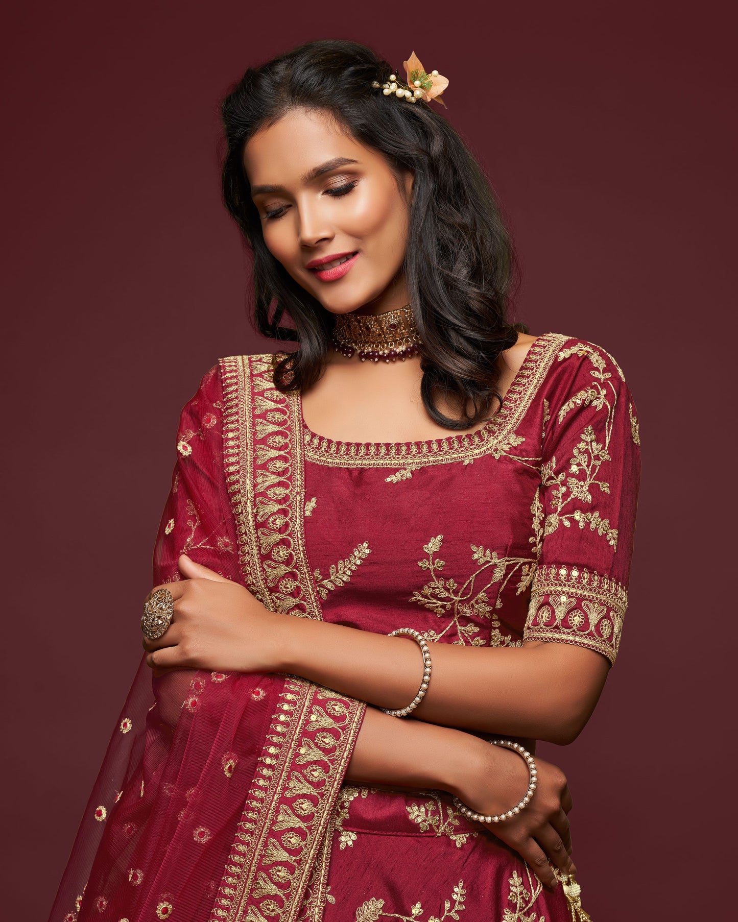 Woman wearing a maroon traditional outfit with gold embroidery on a dark red background