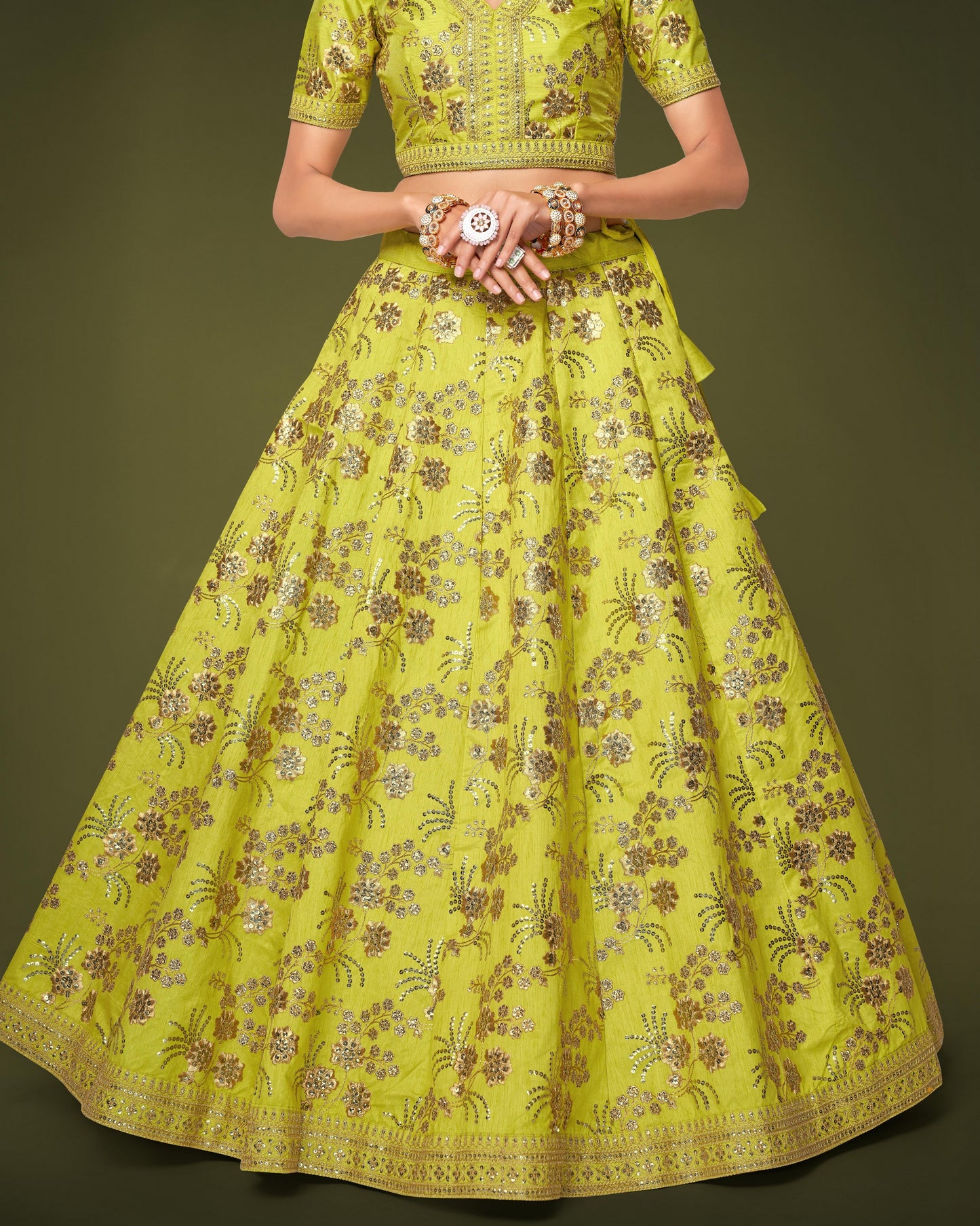 Woman wearing a bright green traditional outfit with floral patterns on a dark background