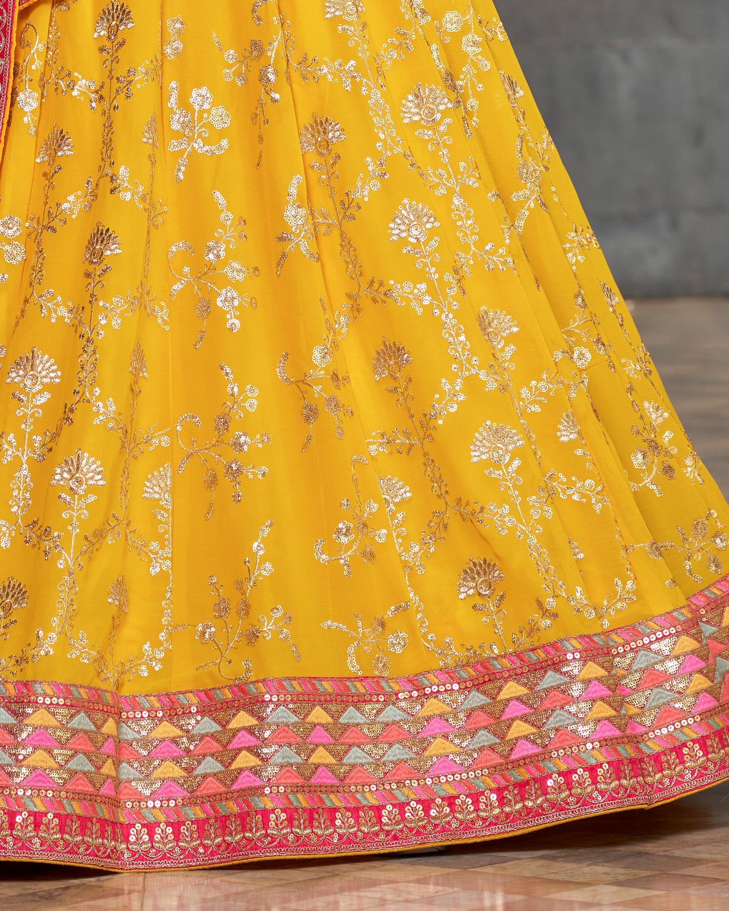 Yellow embroidered fabric with pink and multicolor border on a wooden surface