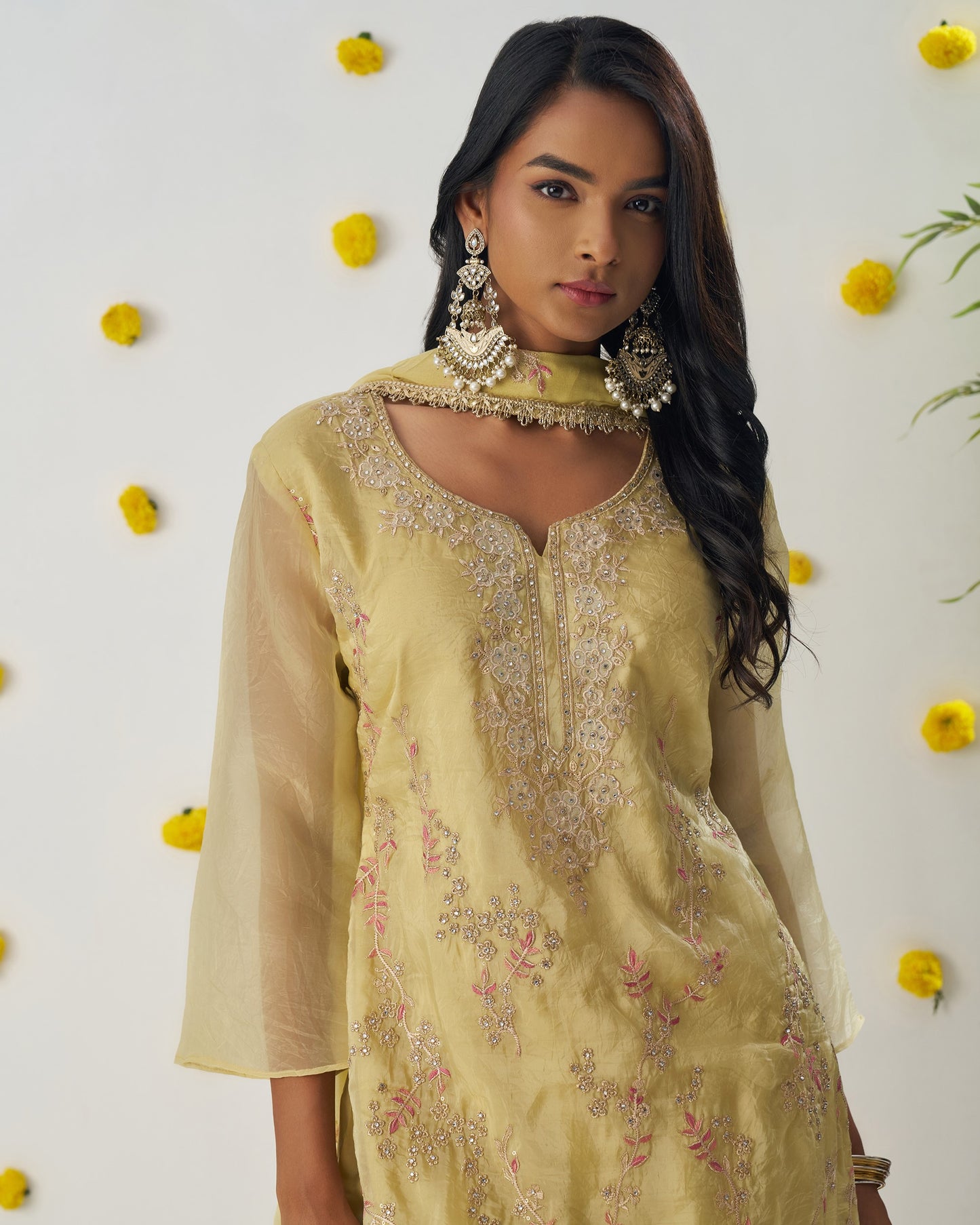 Woman wearing a light yellow embroidered traditional outfit with floral decorations in the background
