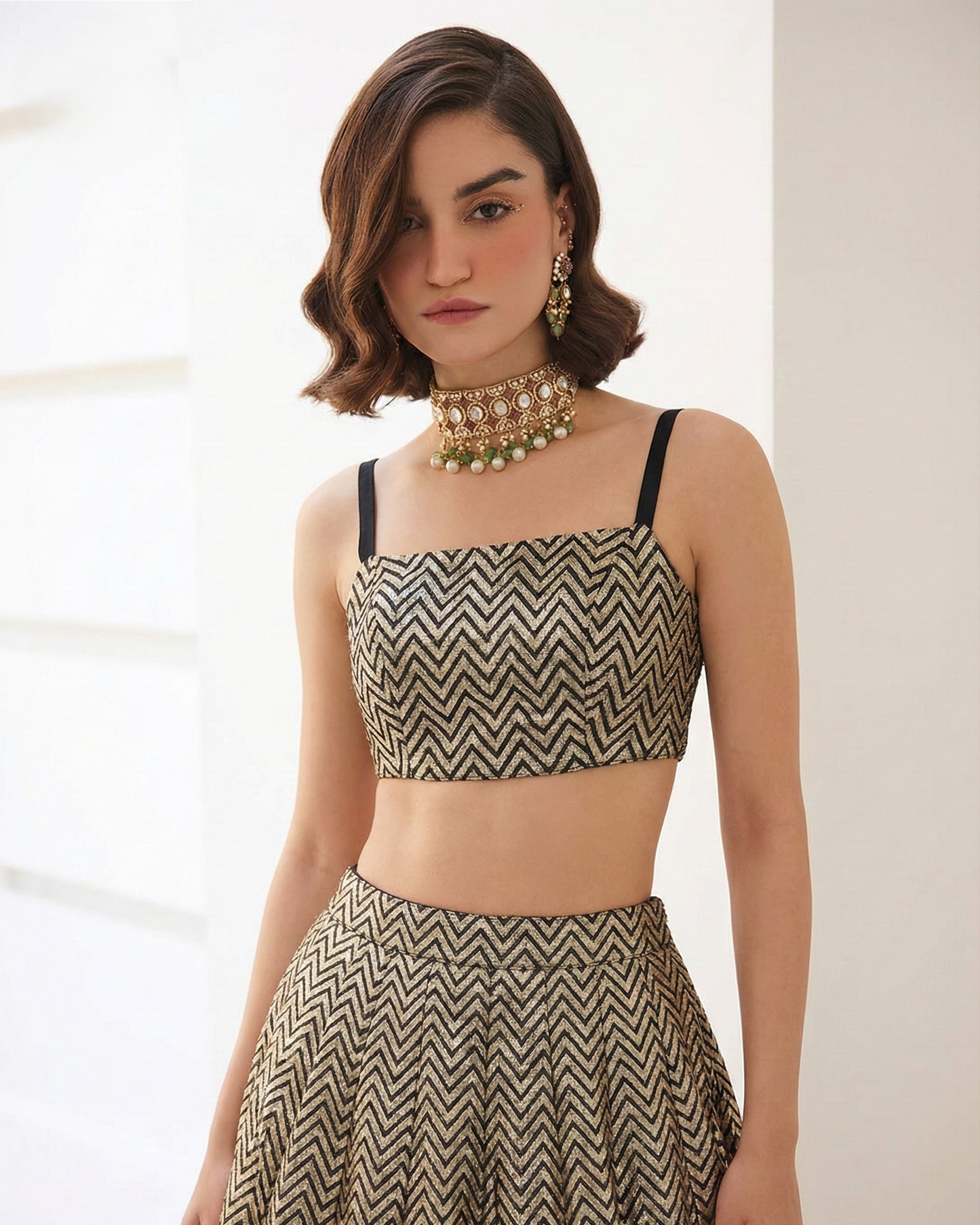 Woman wearing a patterned top and skirt set with gold jewelry against a neutral background
