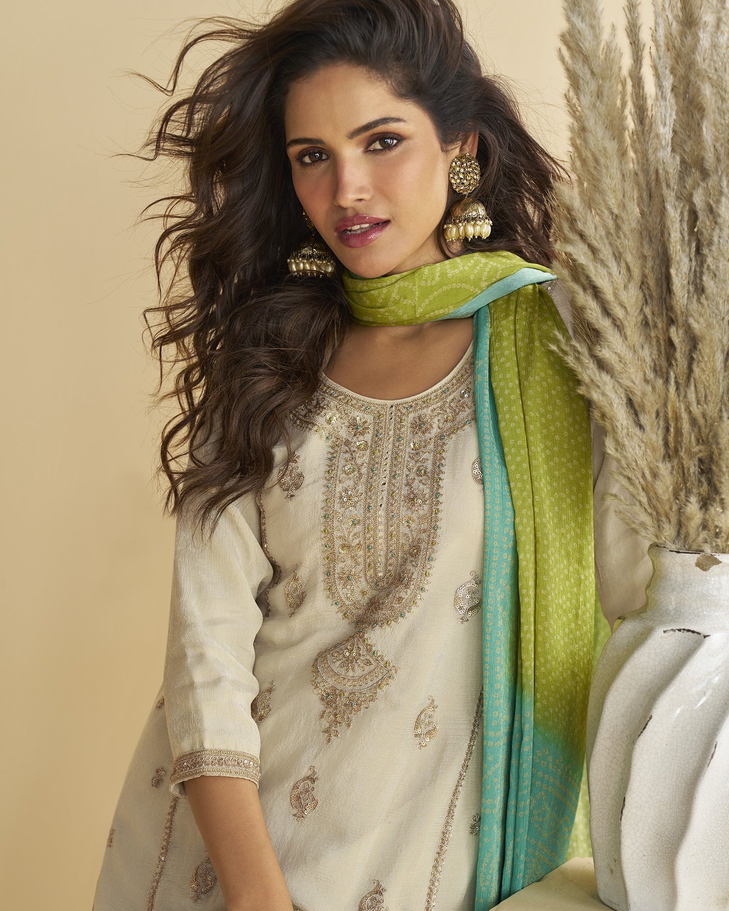 Woman wearing a traditional outfit with a green scarf against a neutral background