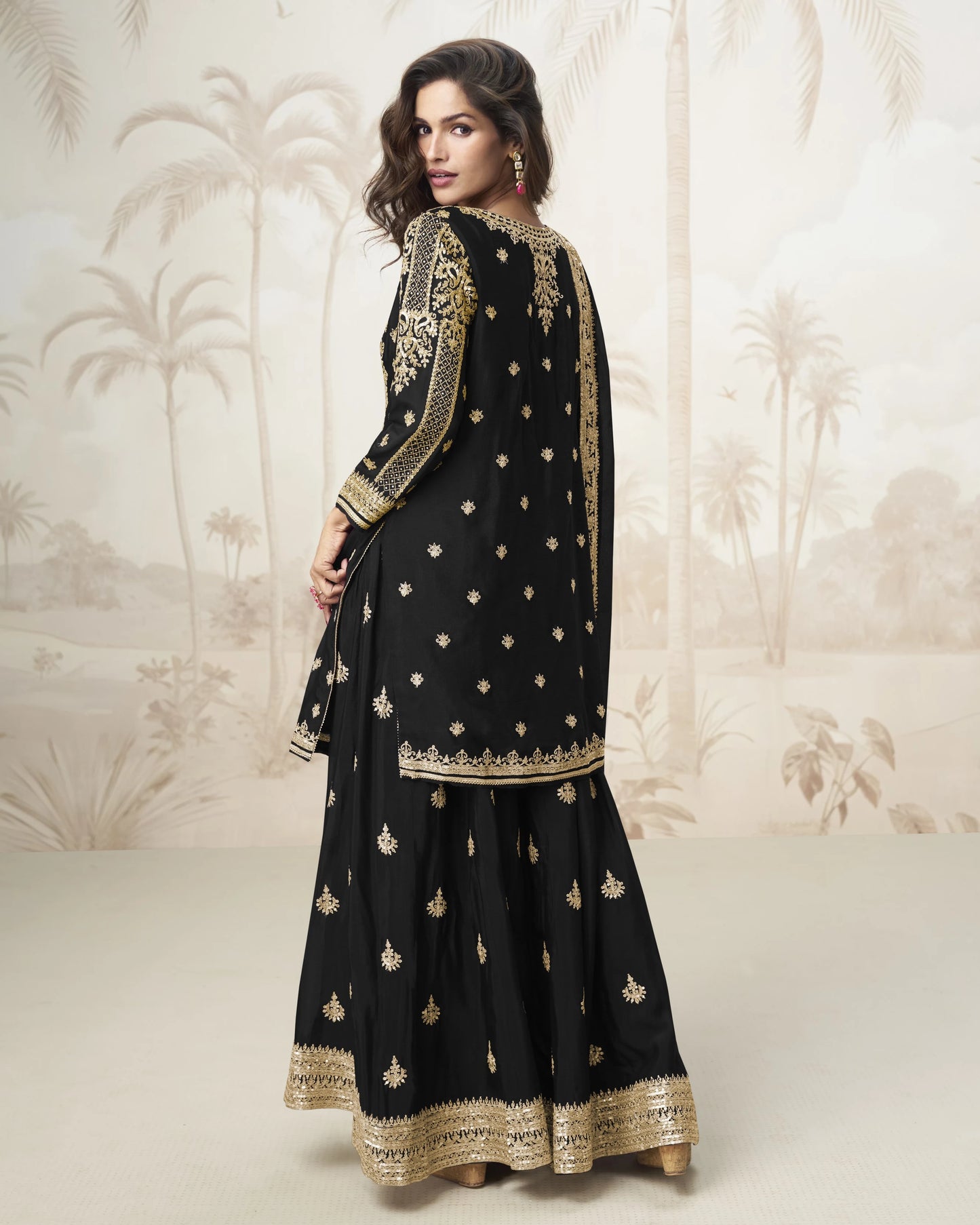 Woman wearing a black traditional outfit with gold embroidery against a neutral background
