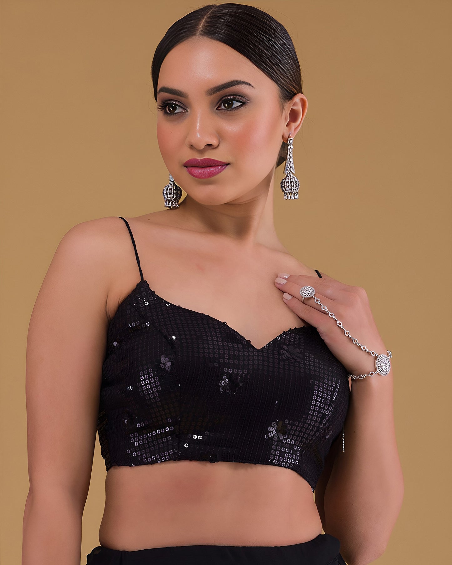 Woman wearing a black sequined top with jewelry on a beige background