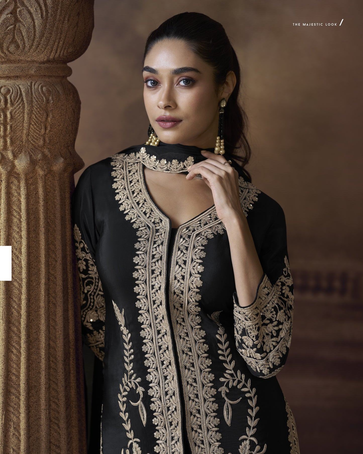 Woman wearing a black and gold embroidered traditional outfit against a warm-toned background.